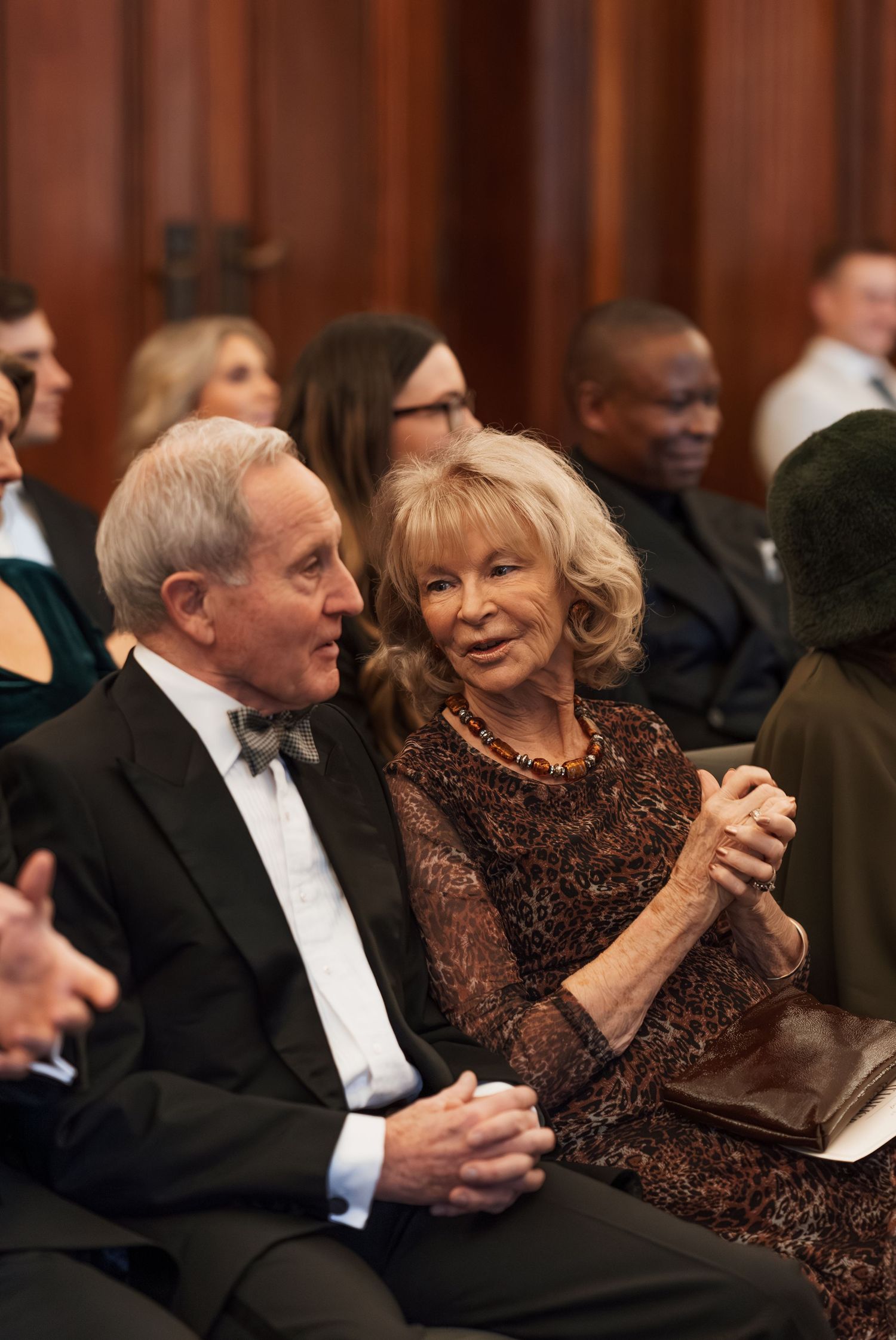 Formal event gathering in wood-paneled room with elegant evening attire.