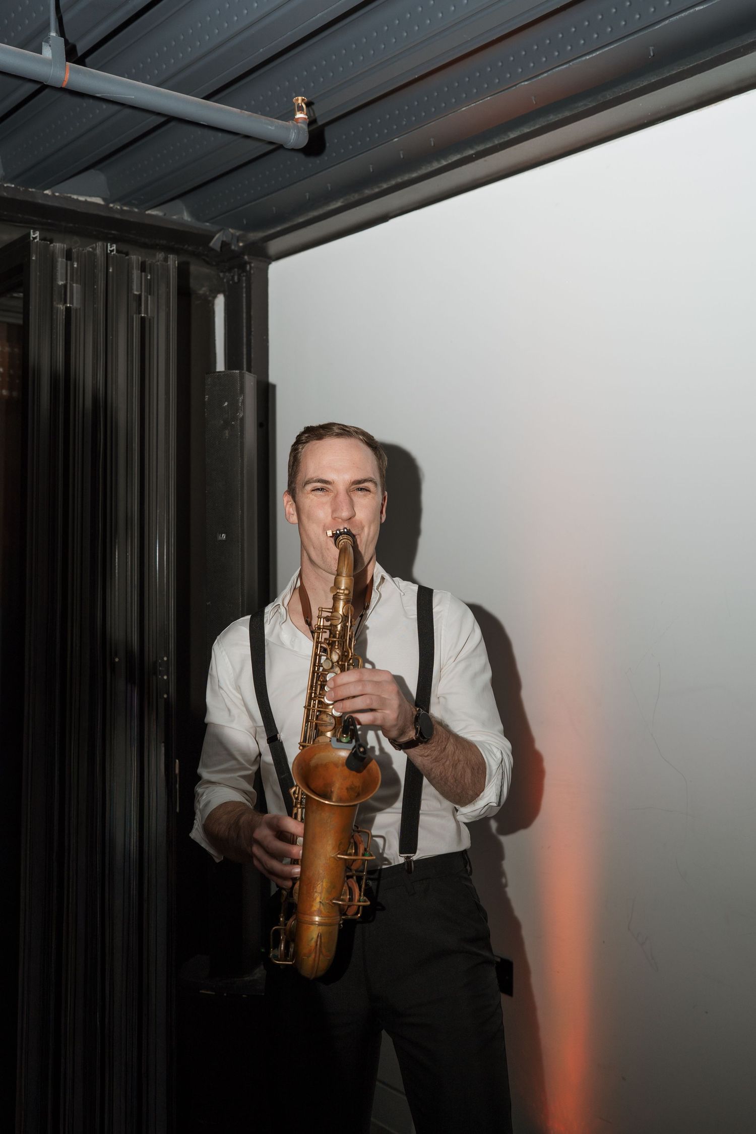 Musician playing saxophone in dramatic lighting during an indoor performance.