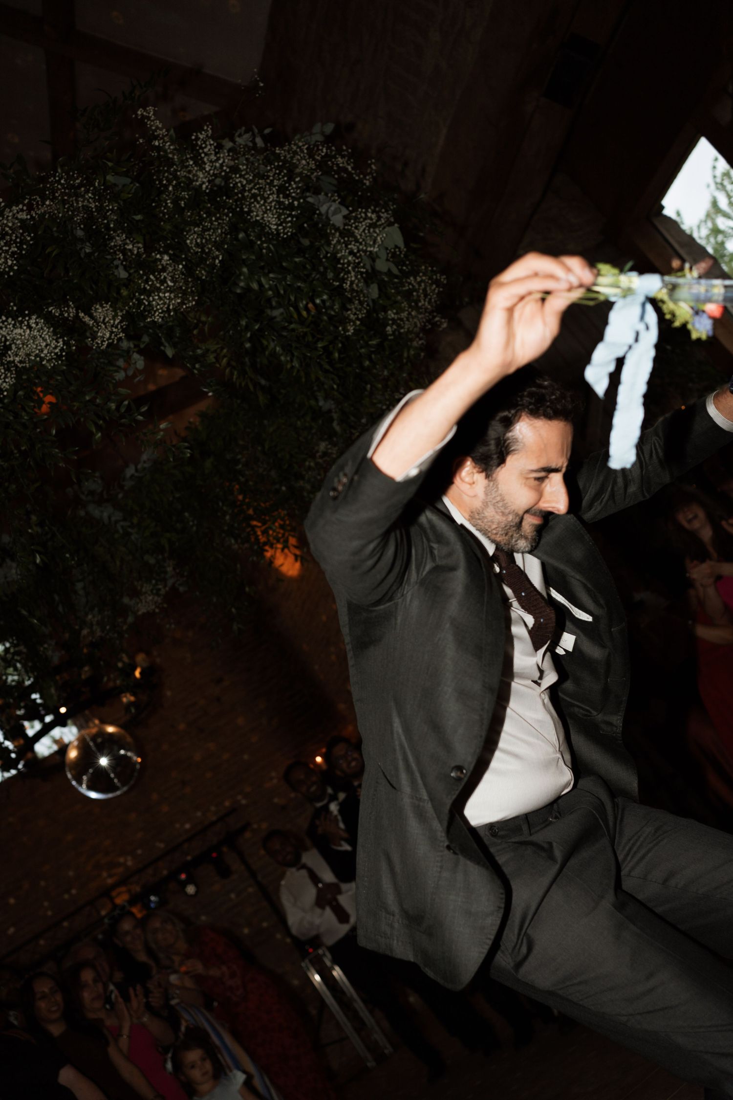 Guest in dark suit dances enthusiastically at indoor wedding reception.