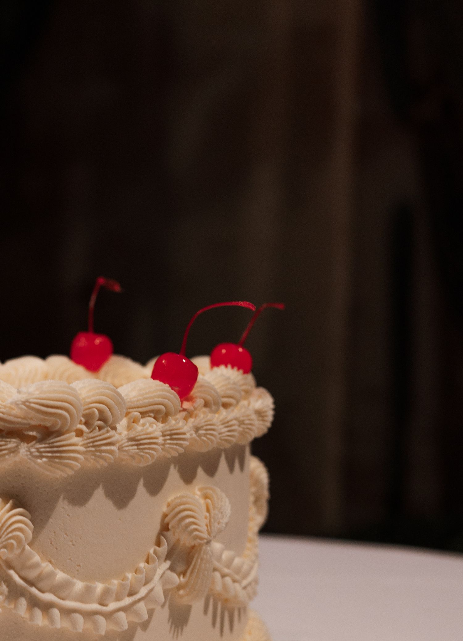 Wedding cake detail with white frosting and red maraschino cherries on top.