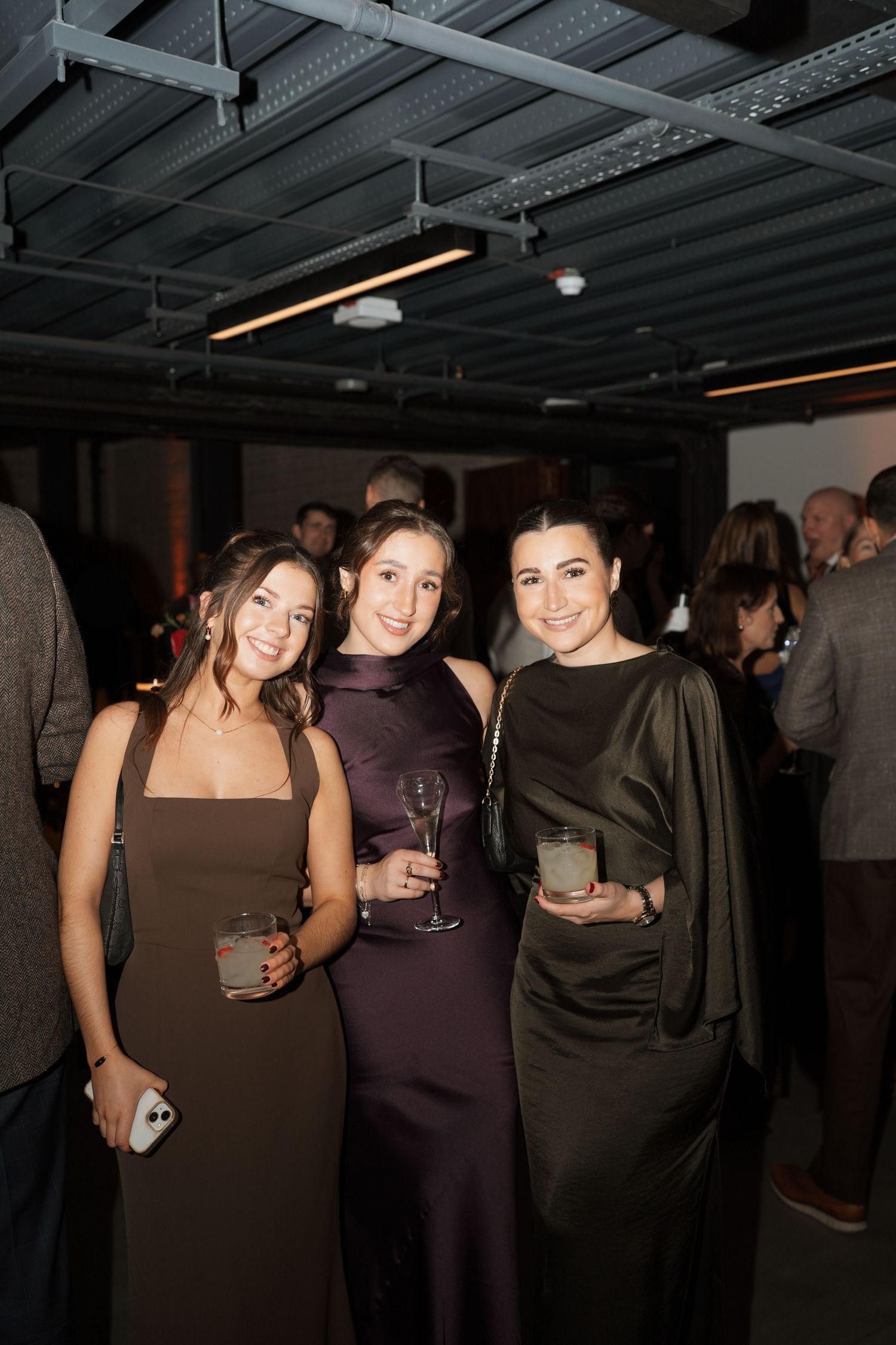 Friends enjoying drinks and conversation at an indoor party in dark formal attire.