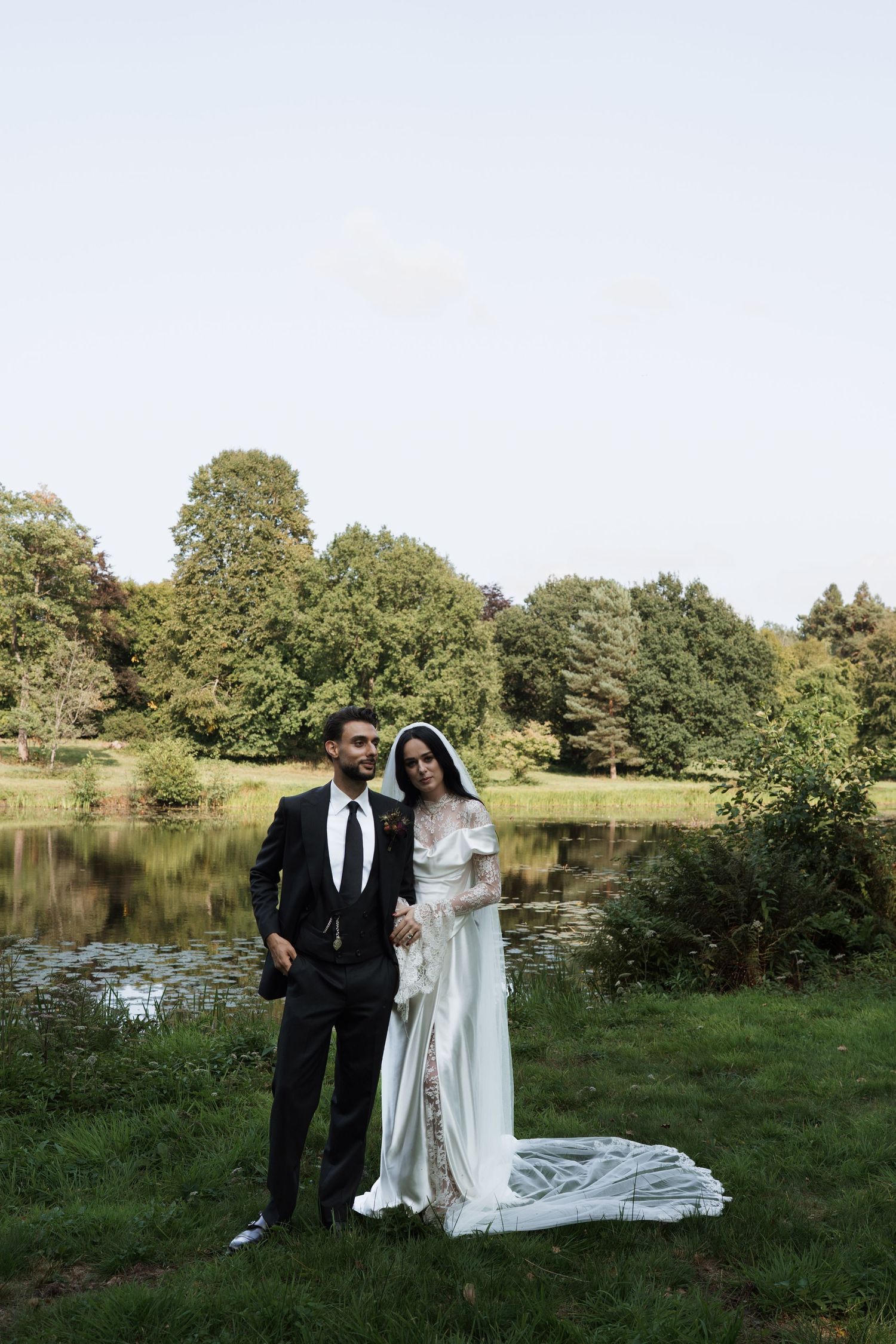 A romantic wedding photo session by a lake with trees in the background.