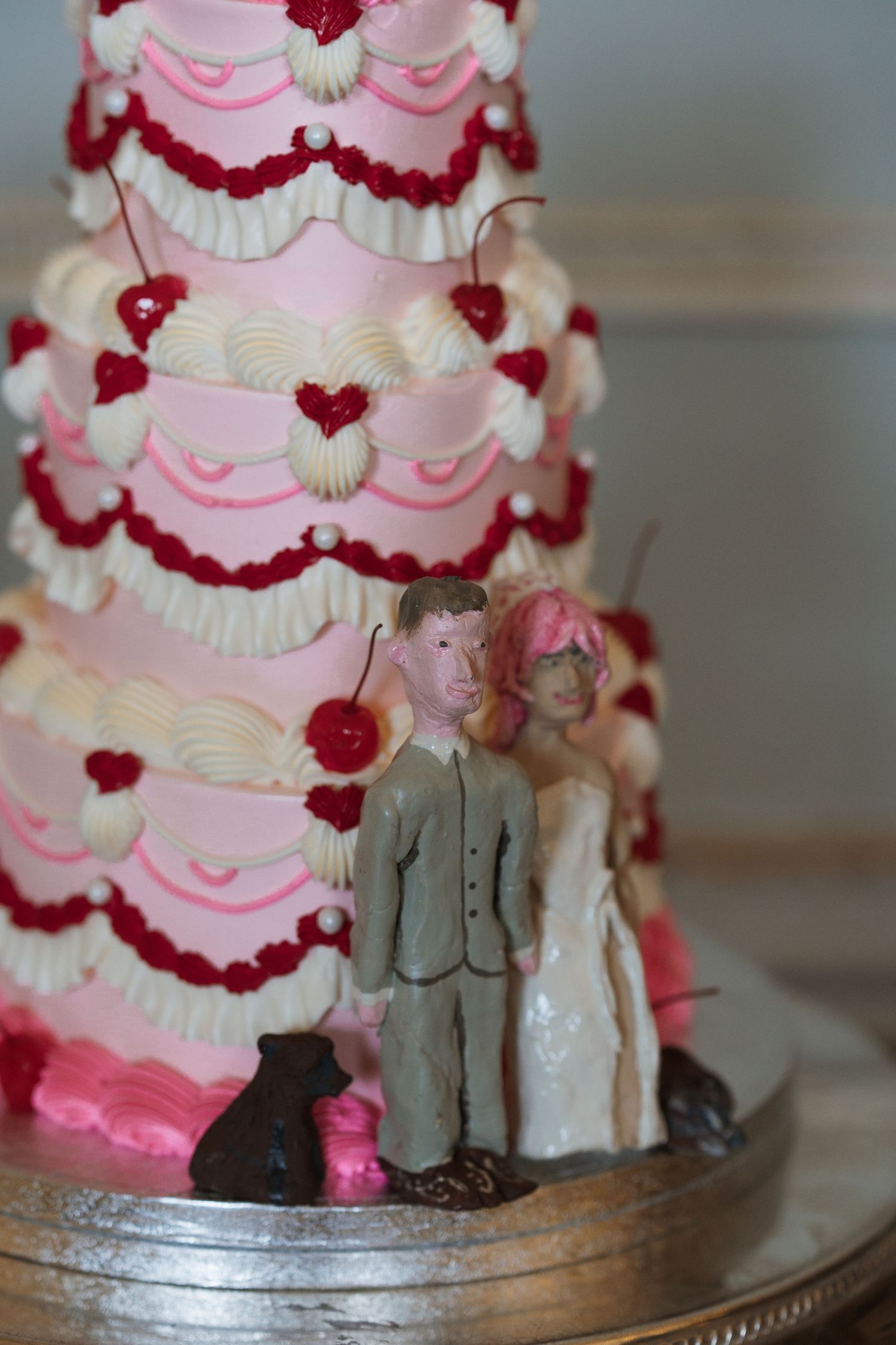 Pink and white wedding cake decorated with red flowers and topped with miniature figurines.