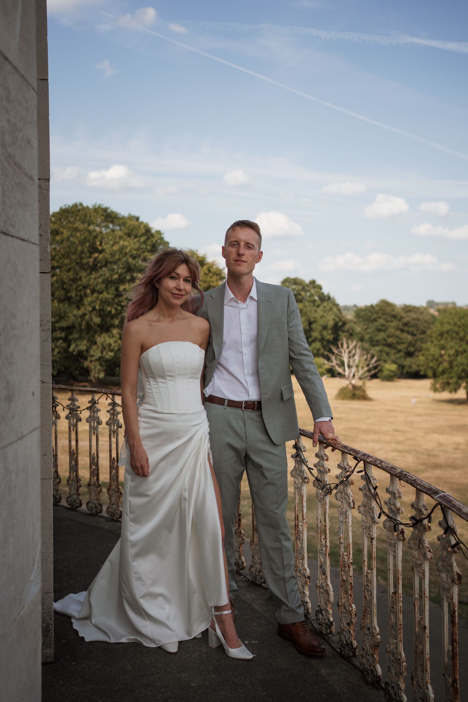 Newlyweds posing together on a balcony with scenic countryside in the background.