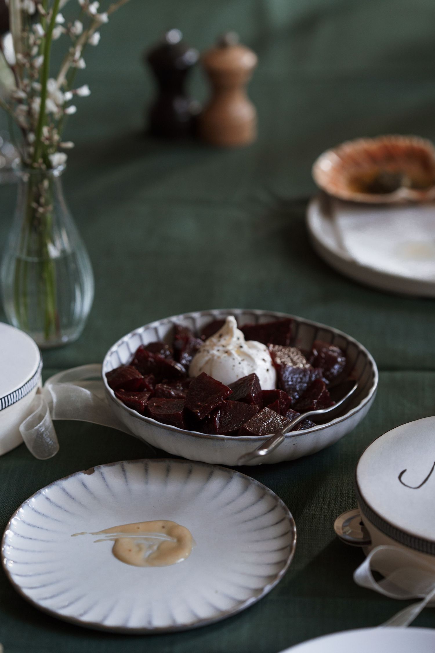White scalloped plates with dark food arranged on a deep green tablecloth.