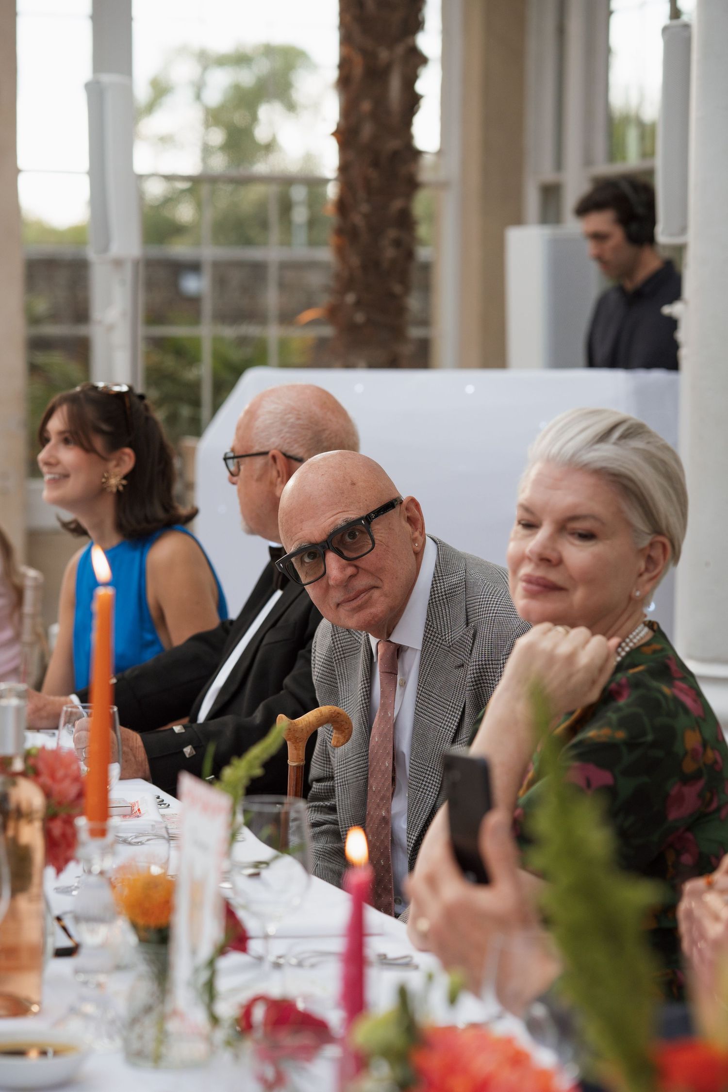 Wedding guests seated at an elegant outdoor dinner table with candles and floral centerpieces.