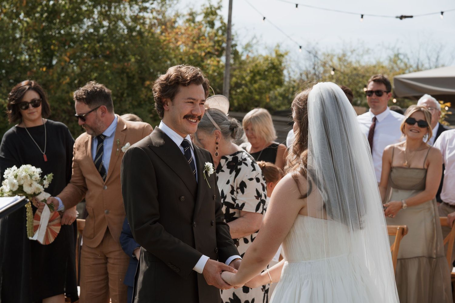 Wedding guests celebrate and laugh during an outdoor ceremony on a sunny day.