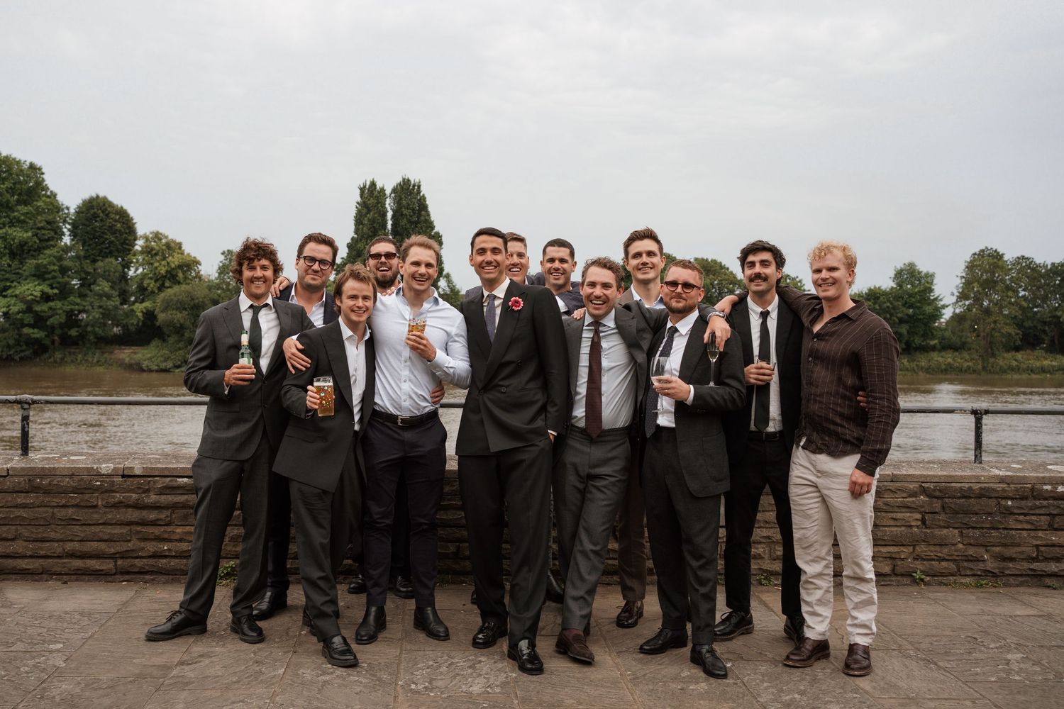 Groomsmen in dark suits pose together outdoors for wedding photos.