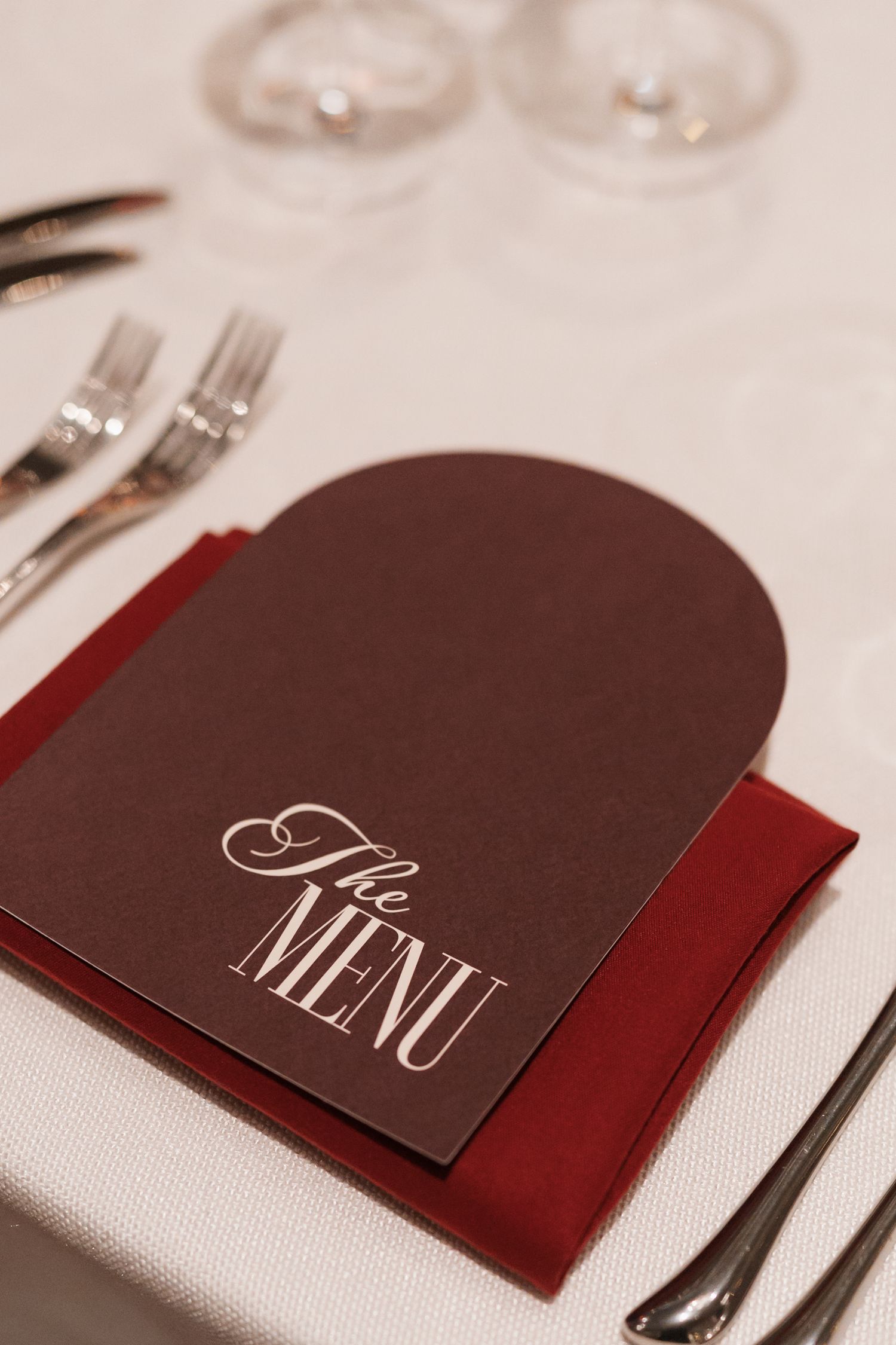Elegant brown and red menu cards with silverware on white tablecloth at formal place settings.
