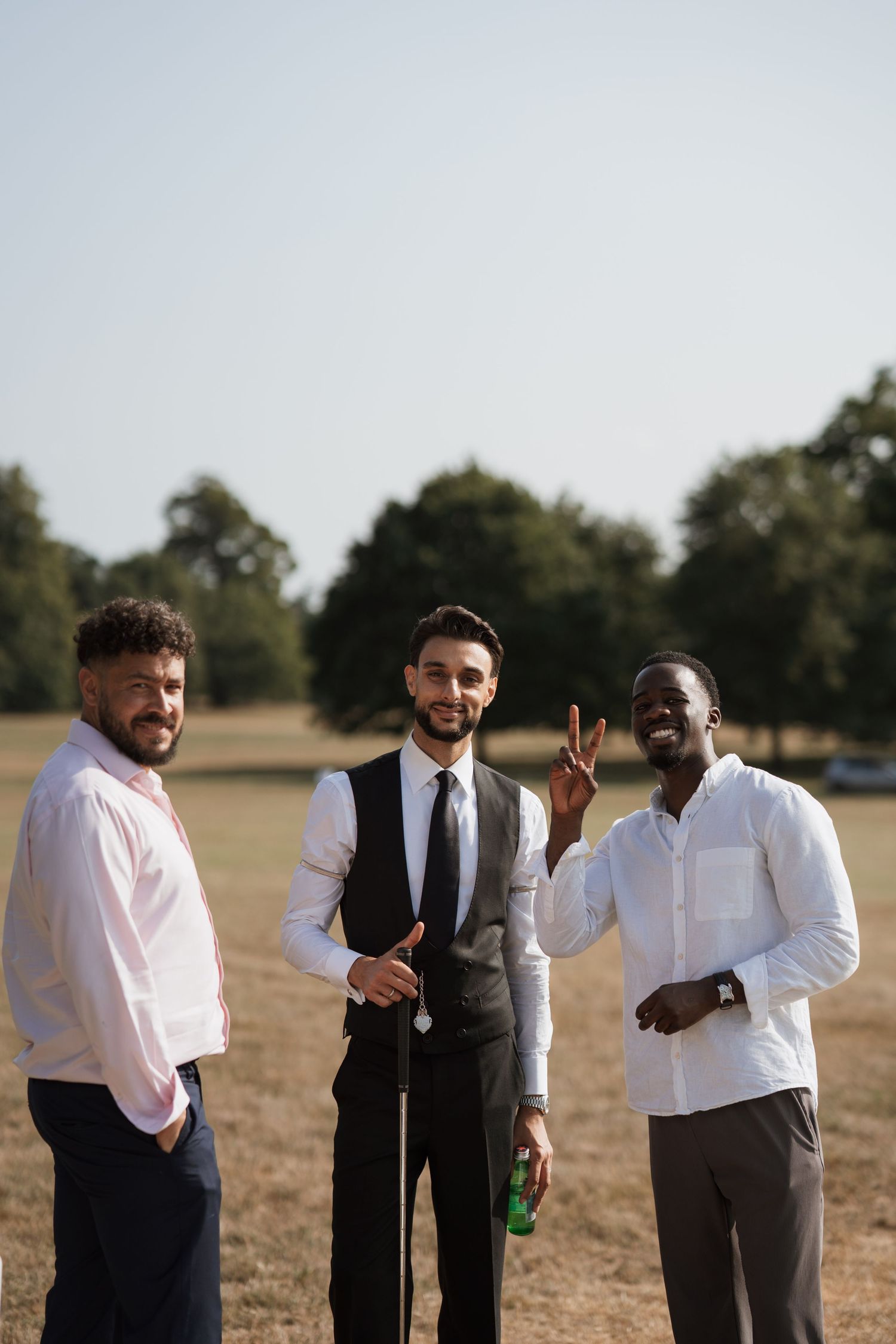 Groomsmen in white shirts and dark ties posing playfully in an outdoor field setting.