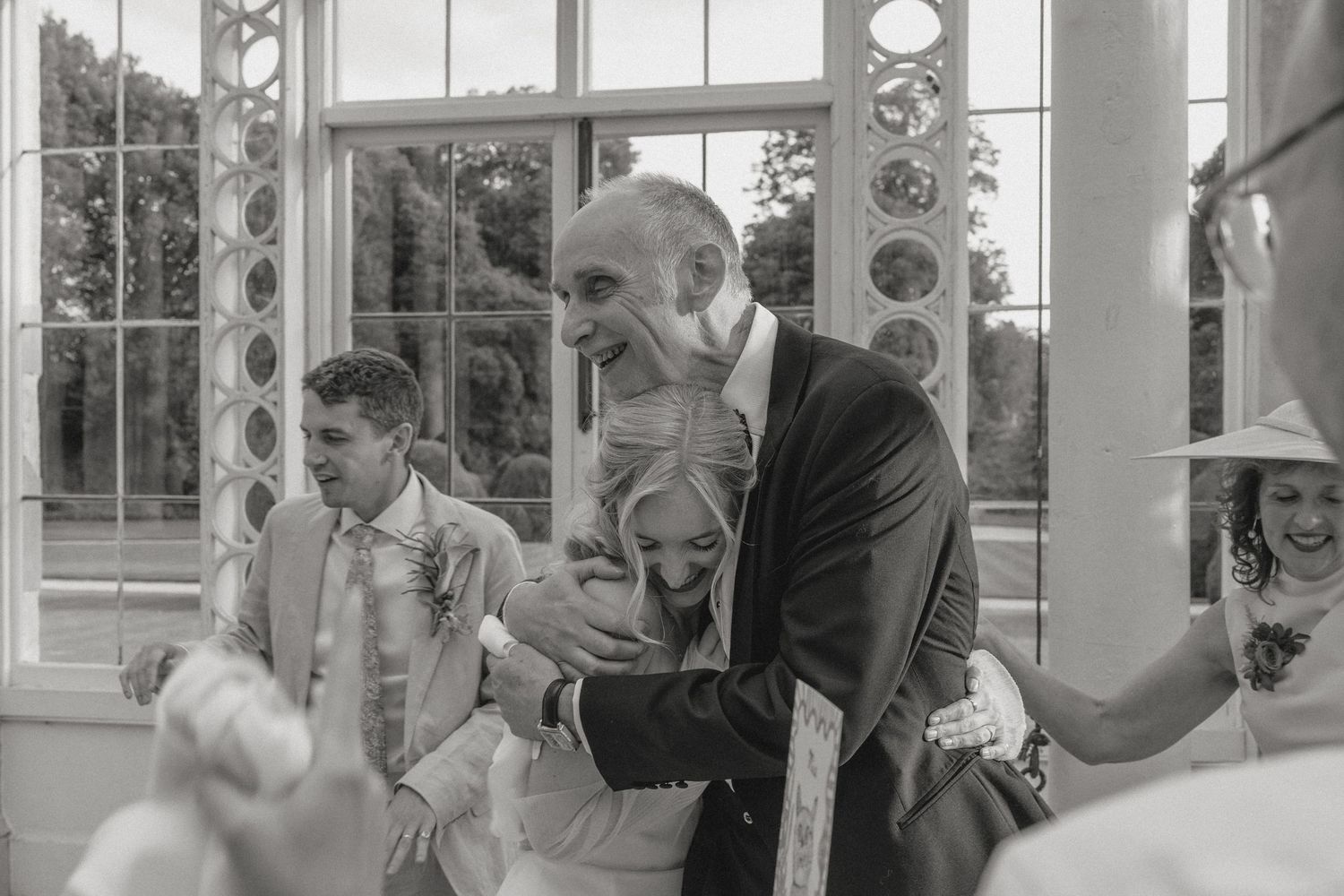 Guests mingling in an elegant conservatory space with large windows and white columns.