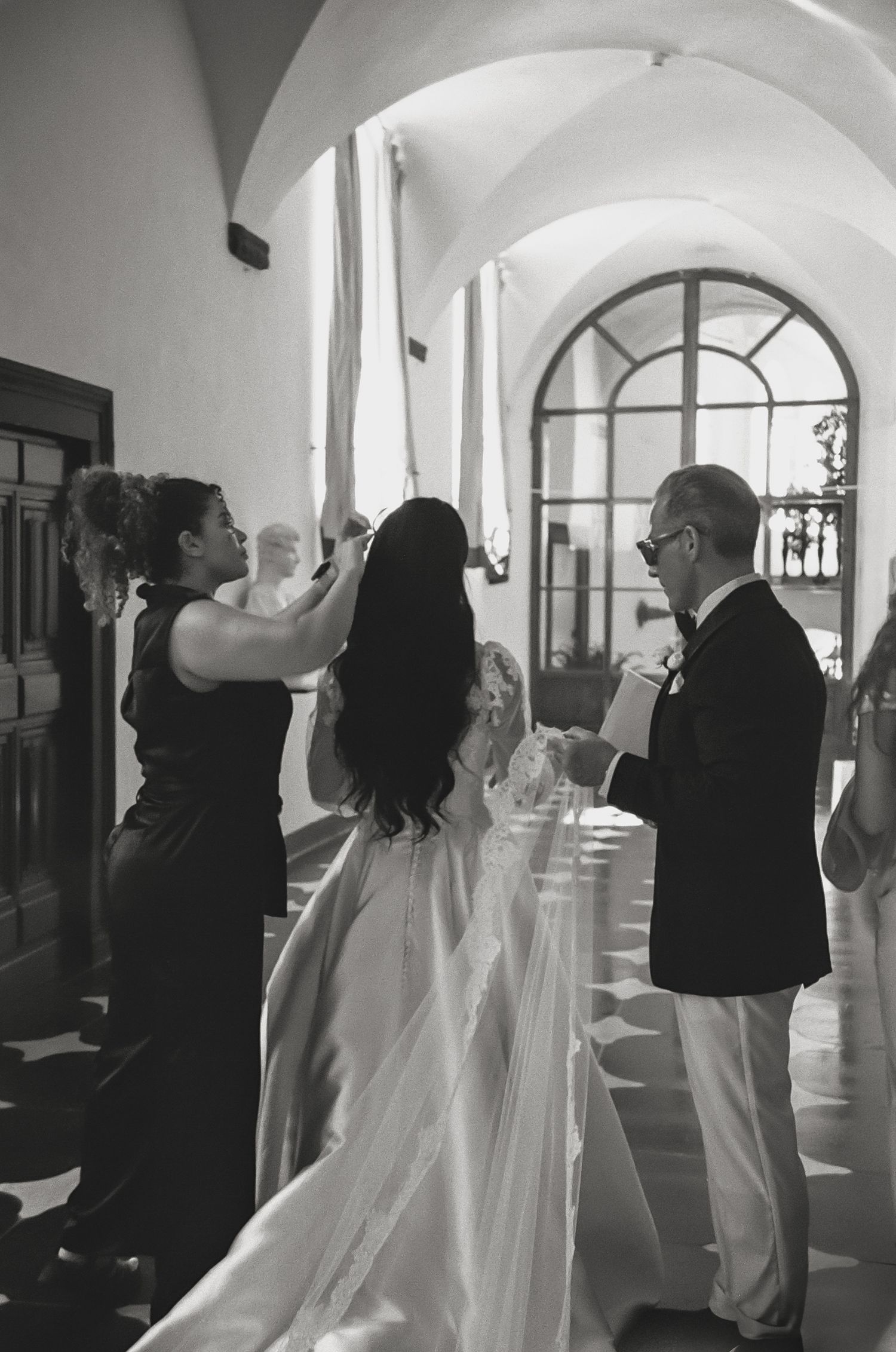 Wedding party dancing together in an elegant white arched hallway during celebration.