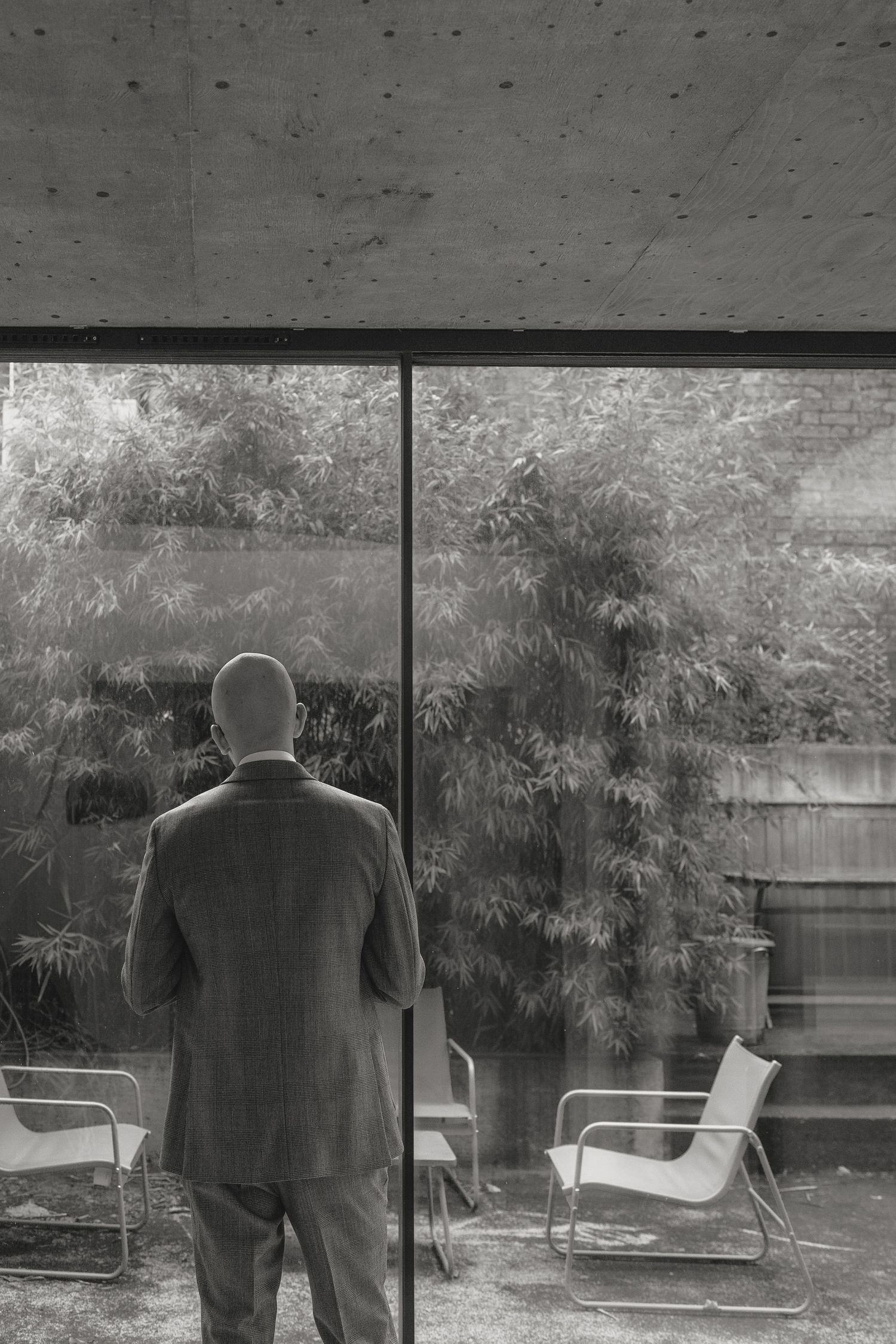 Black and white sequence showing a figure in formal wear looking out large windows with bamboo outside.
