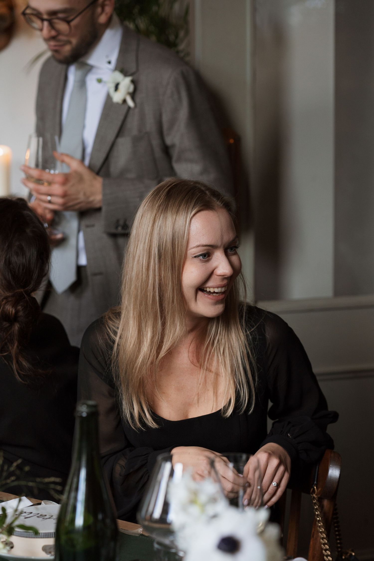 Guests enjoying laughter and conversation at an elegant dinner party with candlelight and wine glasses.