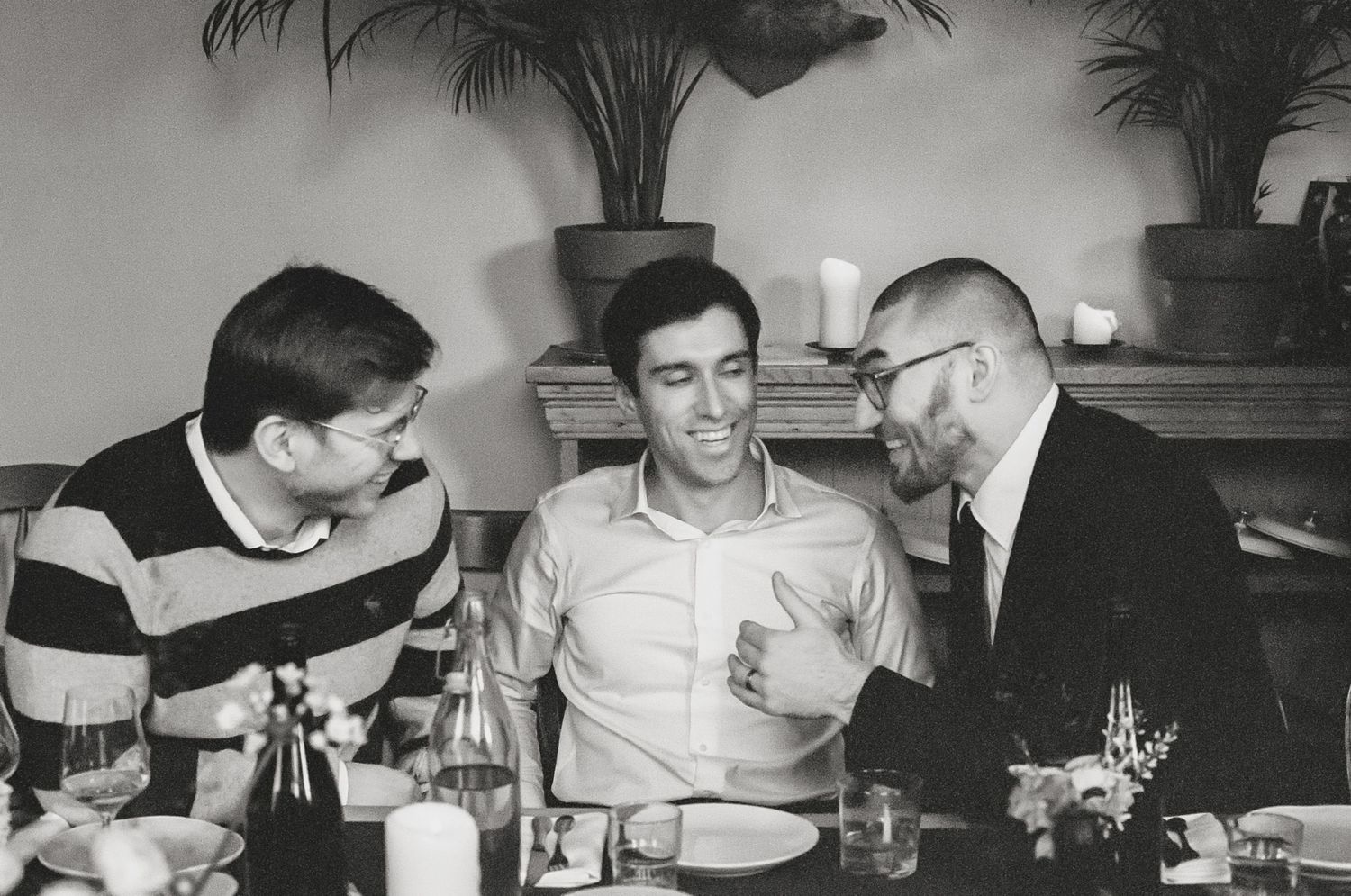Three men sitting together at a dinner table, smiling and conversing in a black and white vintage photo.