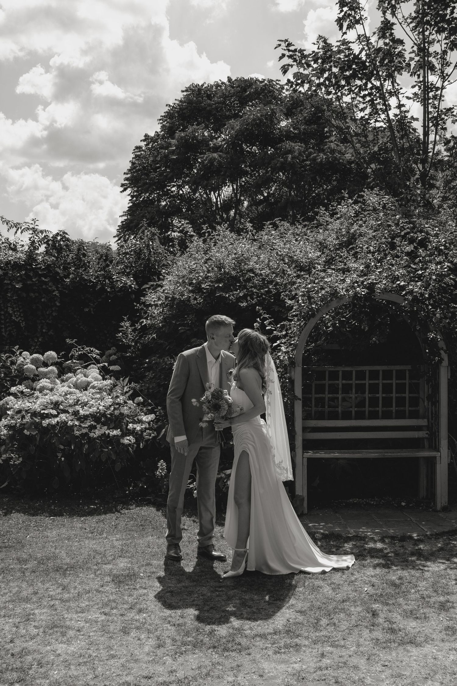 Black and white wedding photo of couples standing together in a garden setting.