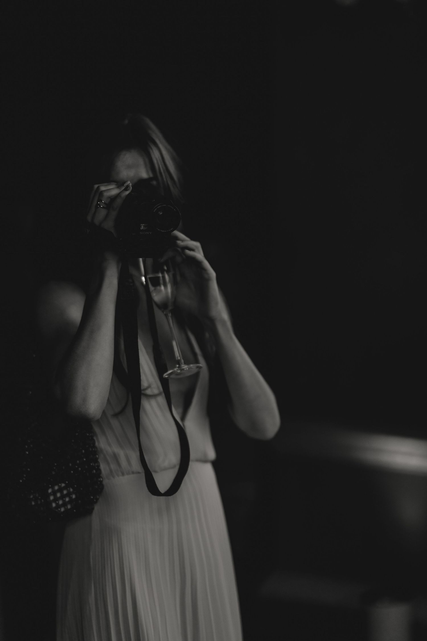 A photographer in a white dress taking photos in a dark setting.