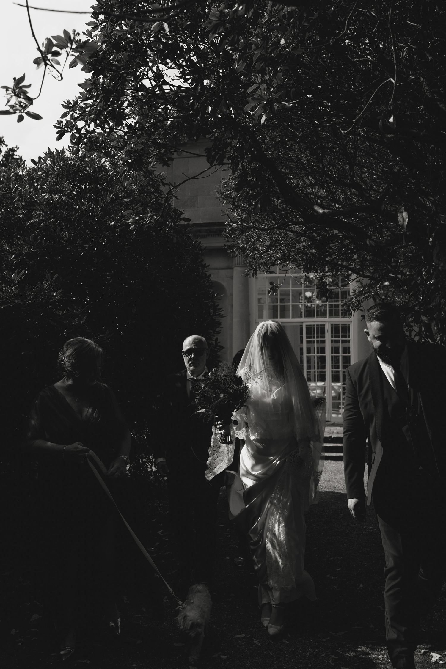 Black and white photo of a wedding celebration in front of a classic house with trees.