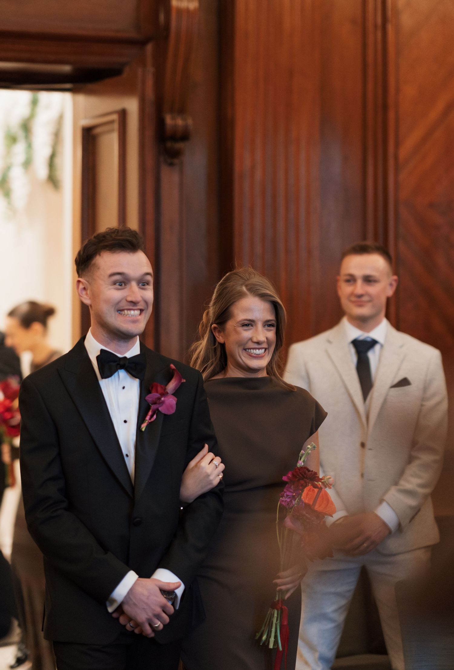 Wedding party members share laughter in a wood-paneled room.