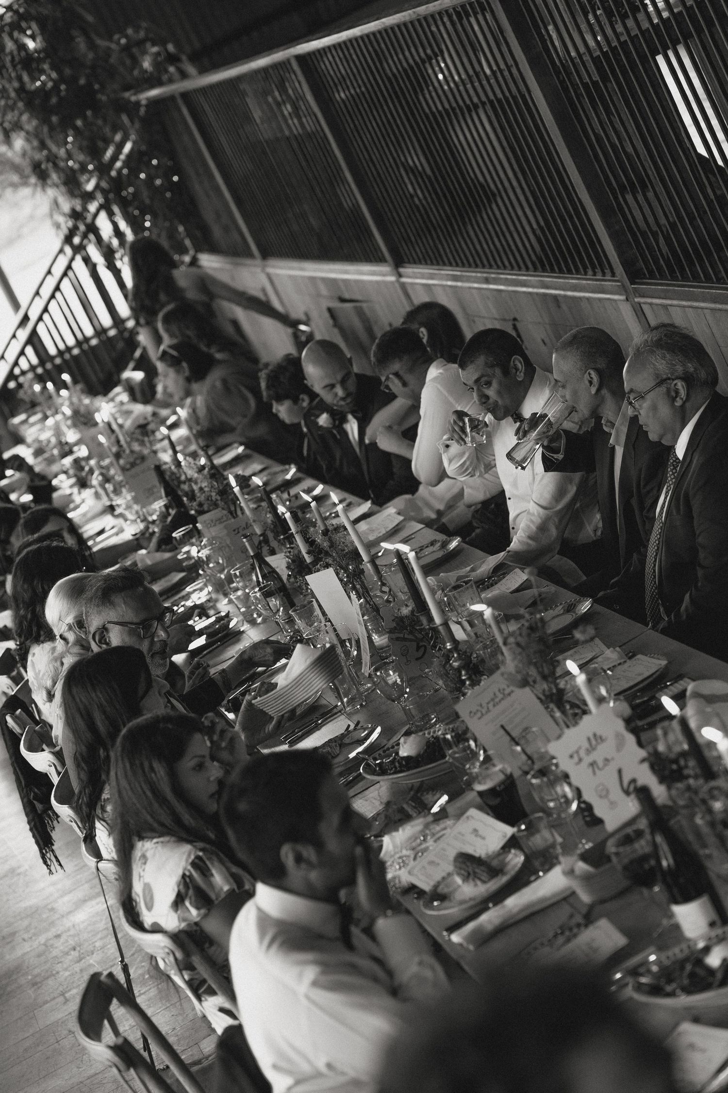 Black and white photo of wedding guests seated at long reception tables.