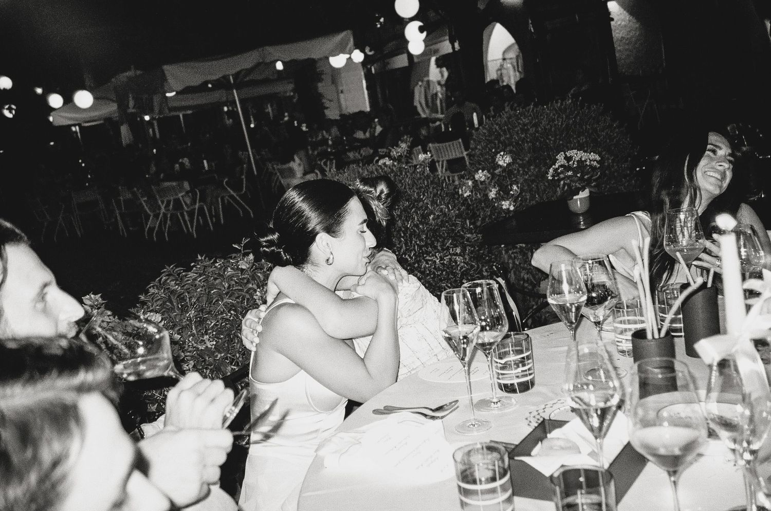 A candid black and white photo of wedding guests enjoying dinner at a reception.
