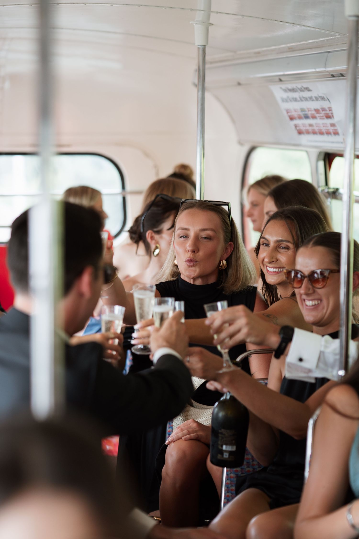 Wedding party celebrates with drinks and laughter inside bright interior space.