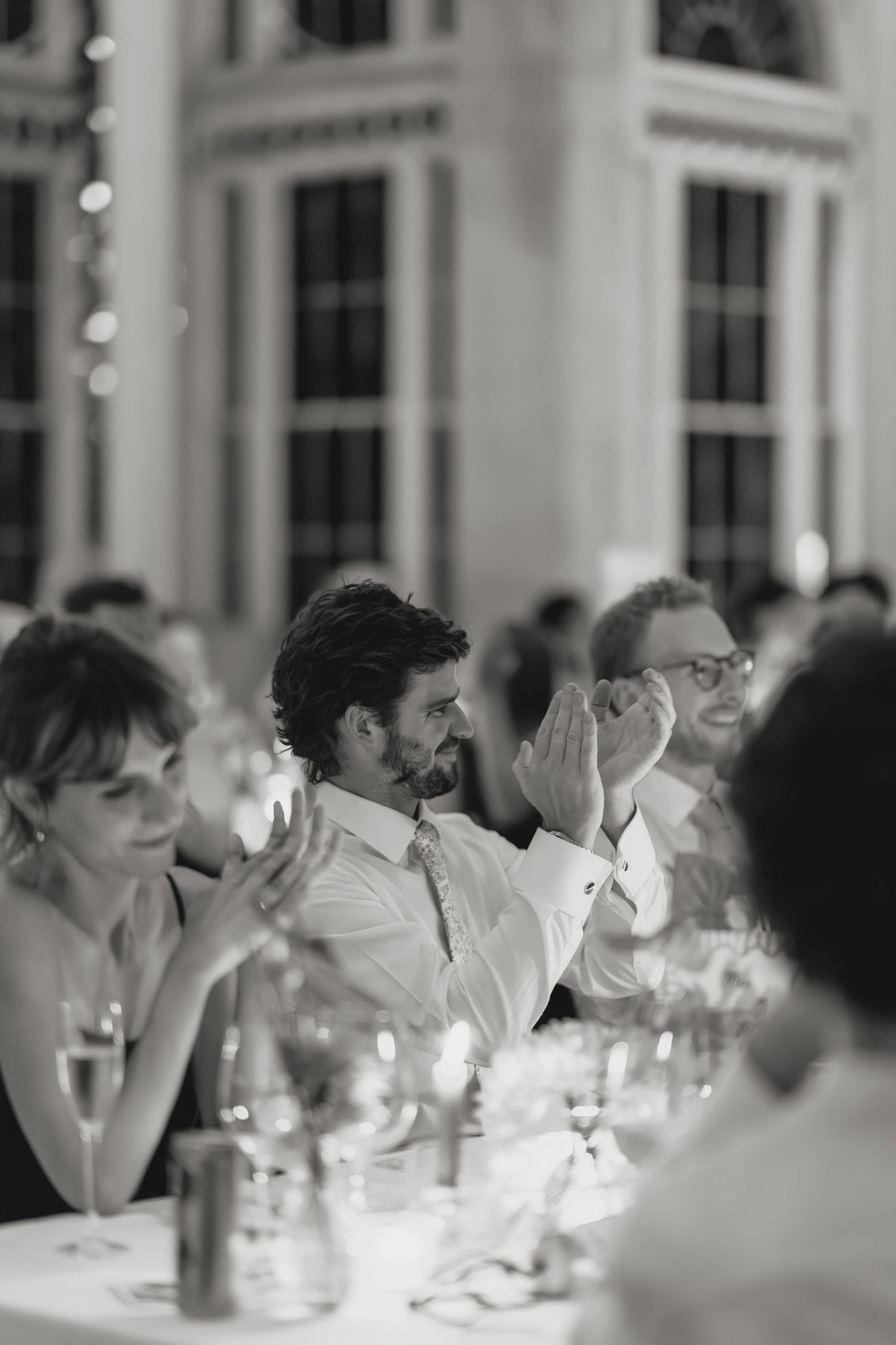 Wedding guests seated at an elegant candlelit dinner table in a formal dining setting.