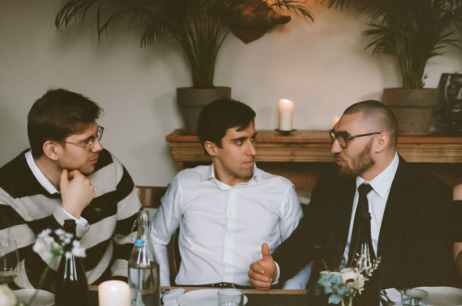Wedding guests engaged in conversation at dimly lit reception dinner.
