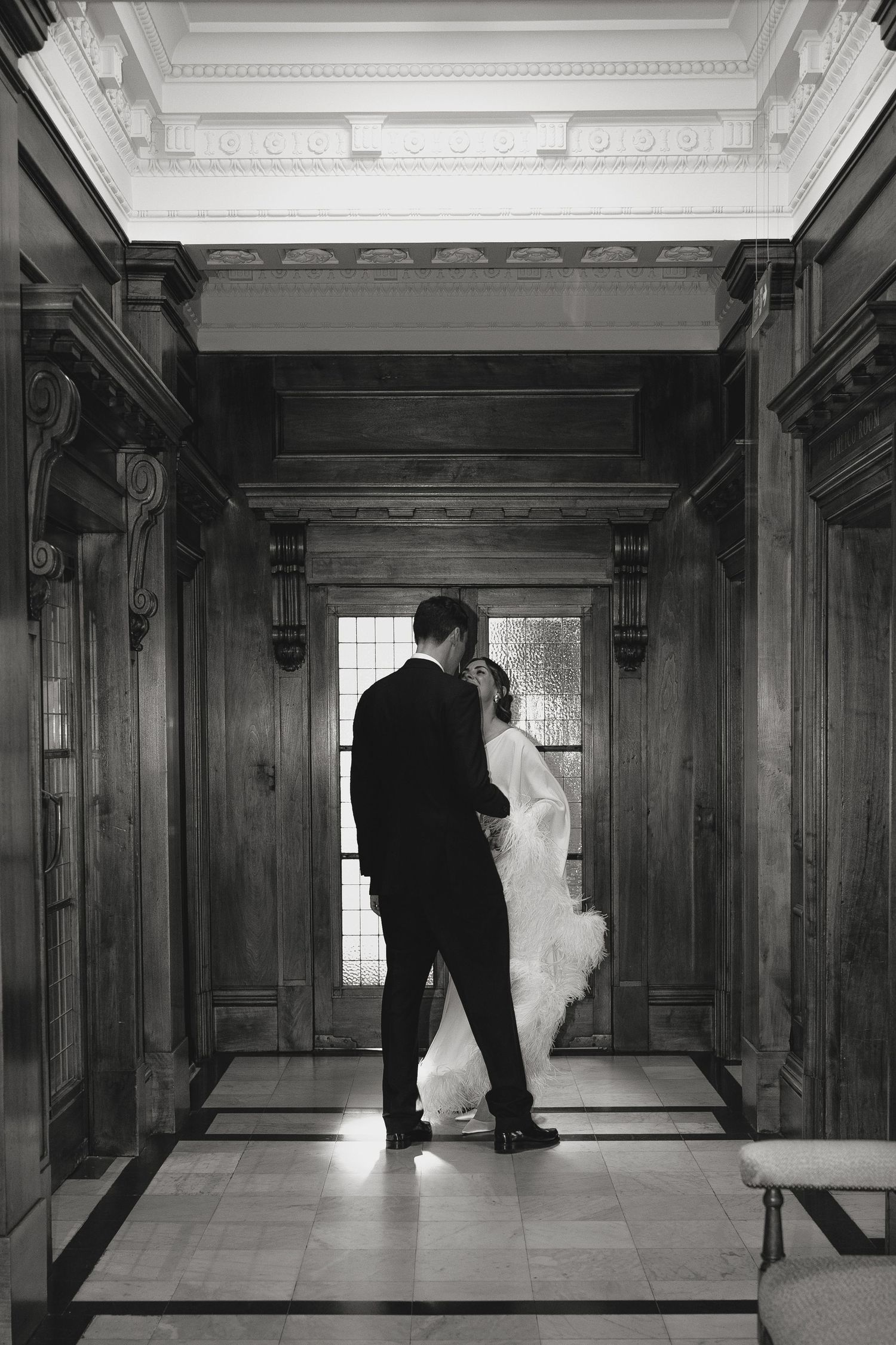 Black and white photo of a hallway with wood paneled walls and elegant lighting.