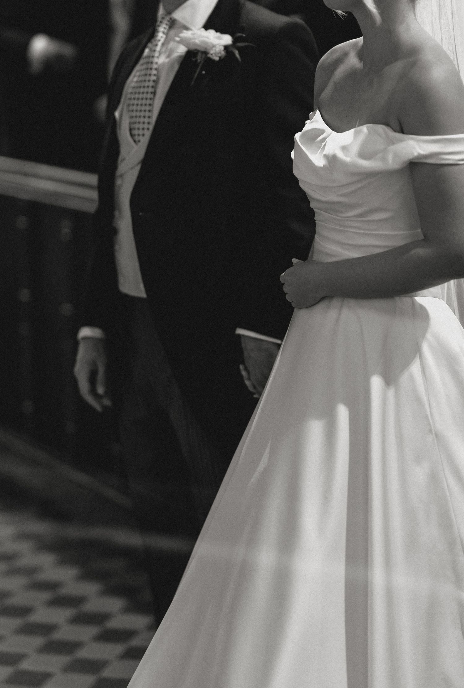 Black and white photo of a bride in a strapless gown standing beside a groom in a suit at a wedding ceremony.