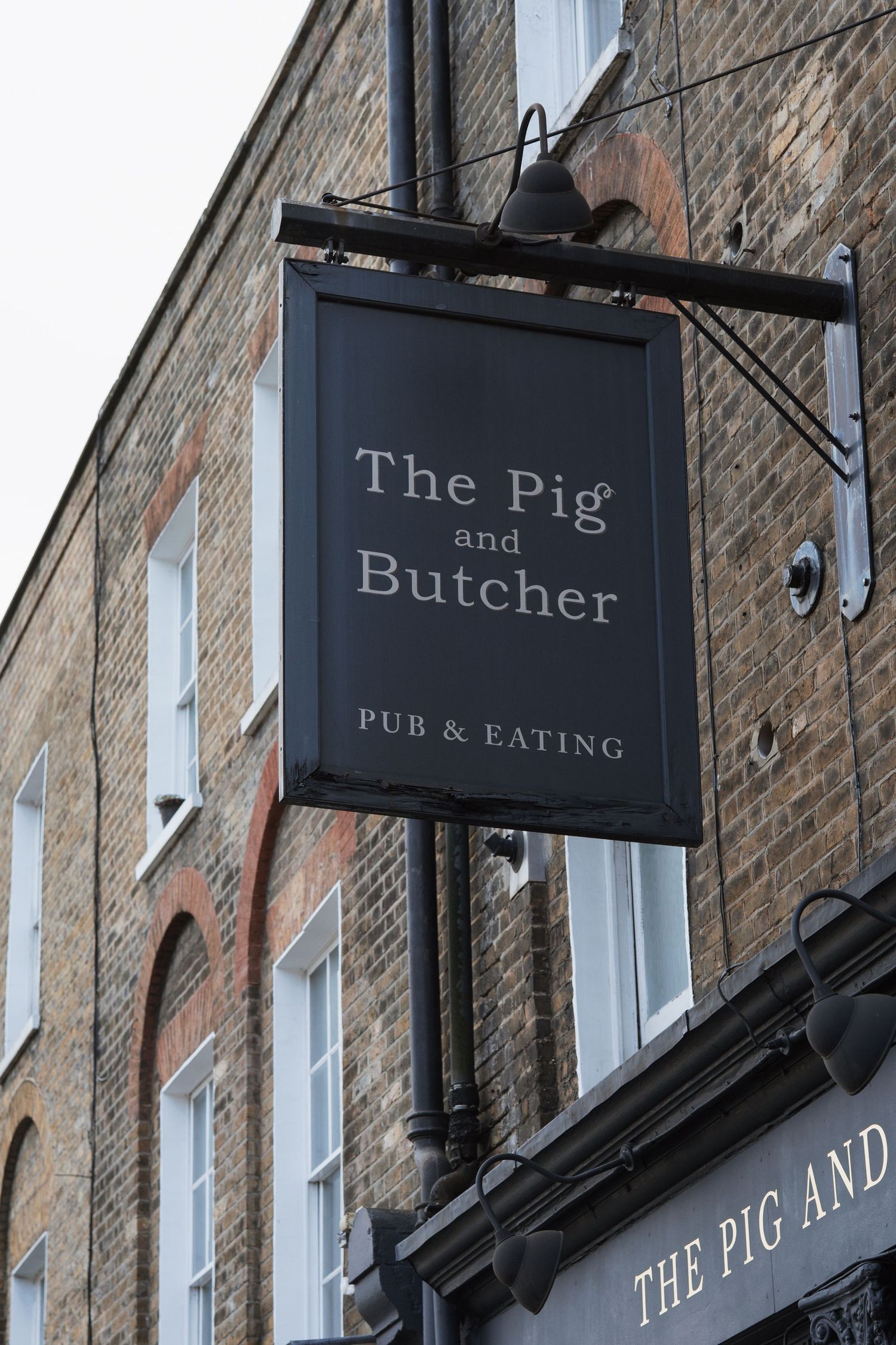 A black pub sign reading 'The Pig and Butcher' mounted on a brick building.