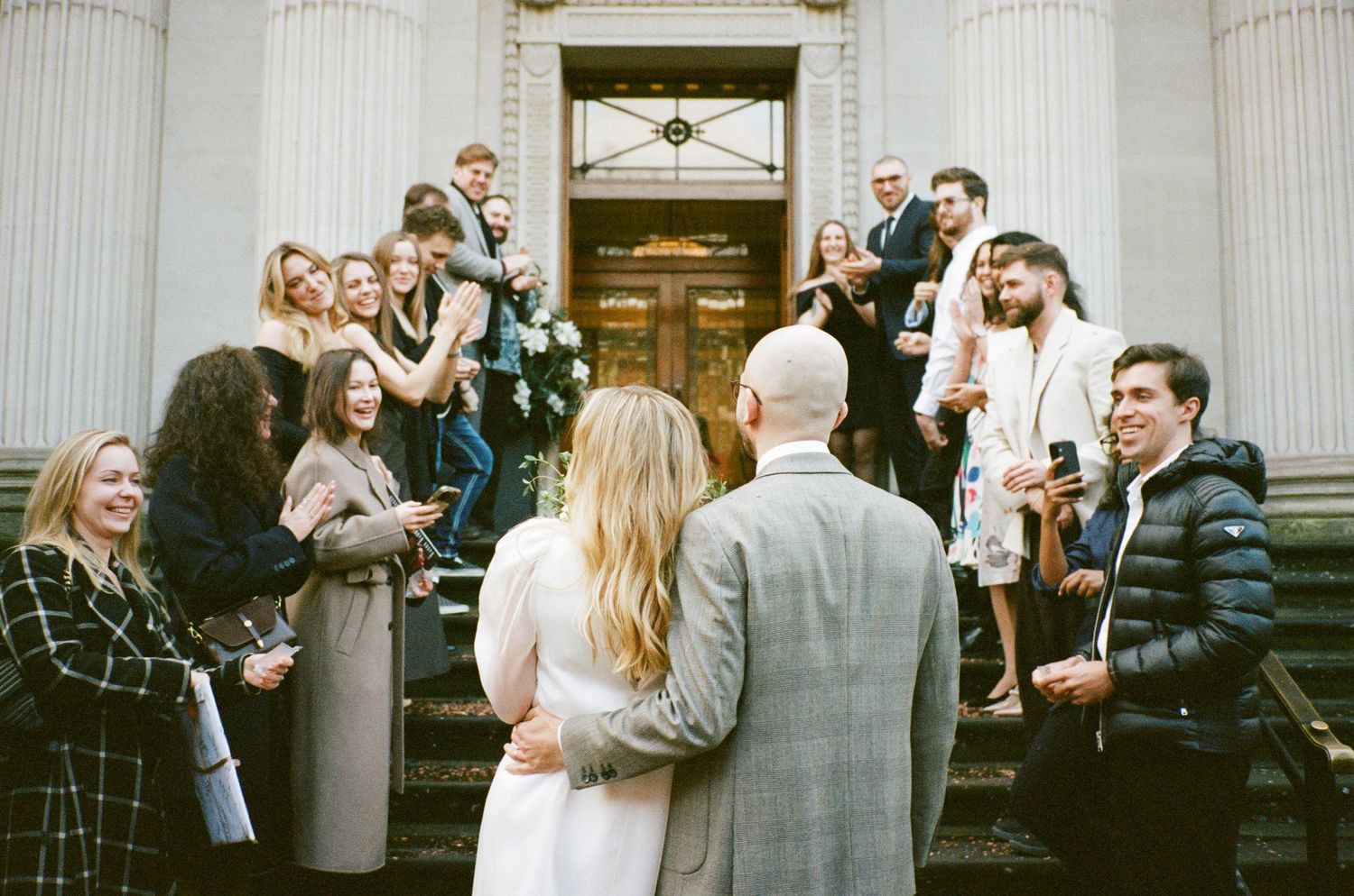 Wedding guests gather on grand stone steps with white columns for outdoor celebration photos.