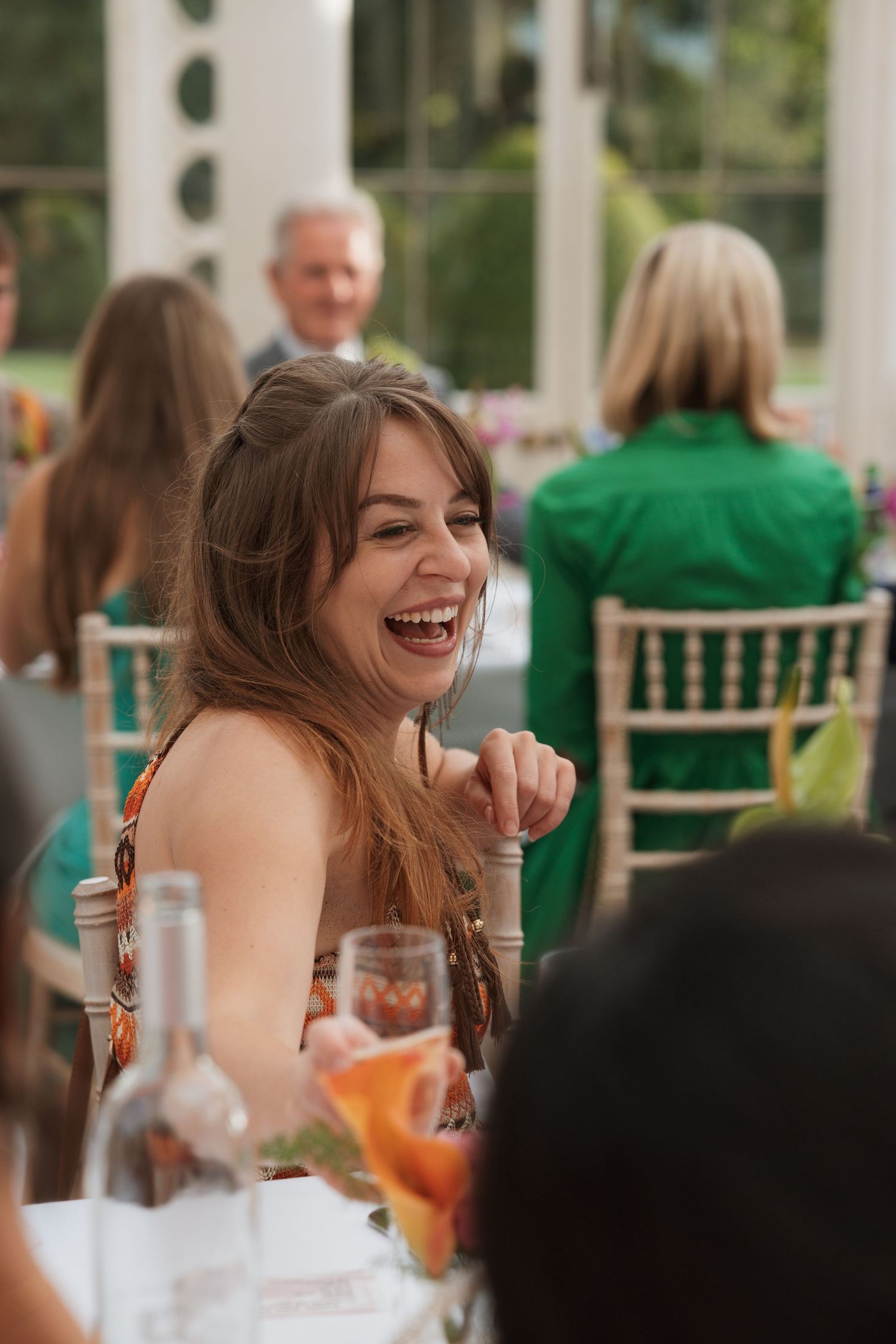 Joyful celebration moments captured during a wedding reception in an elegant glass-walled venue.