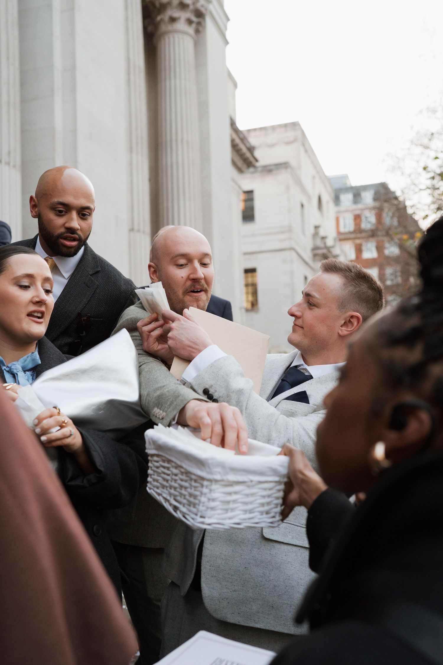 A group struggles playfully with a white fabric outside a columned building.