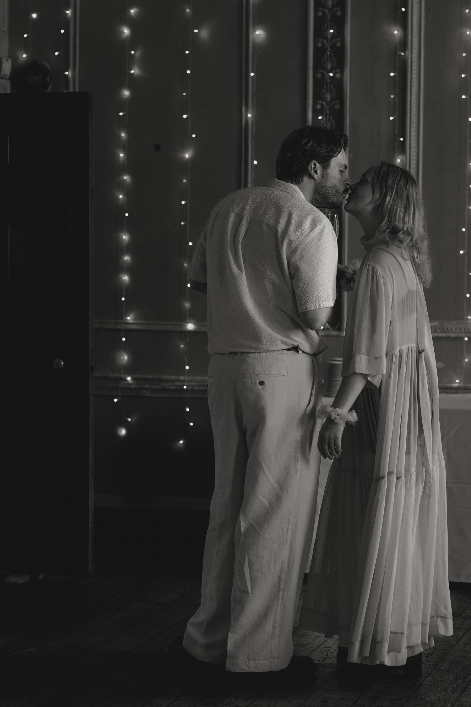 Couple shares intimate moment under string lights at formal event.