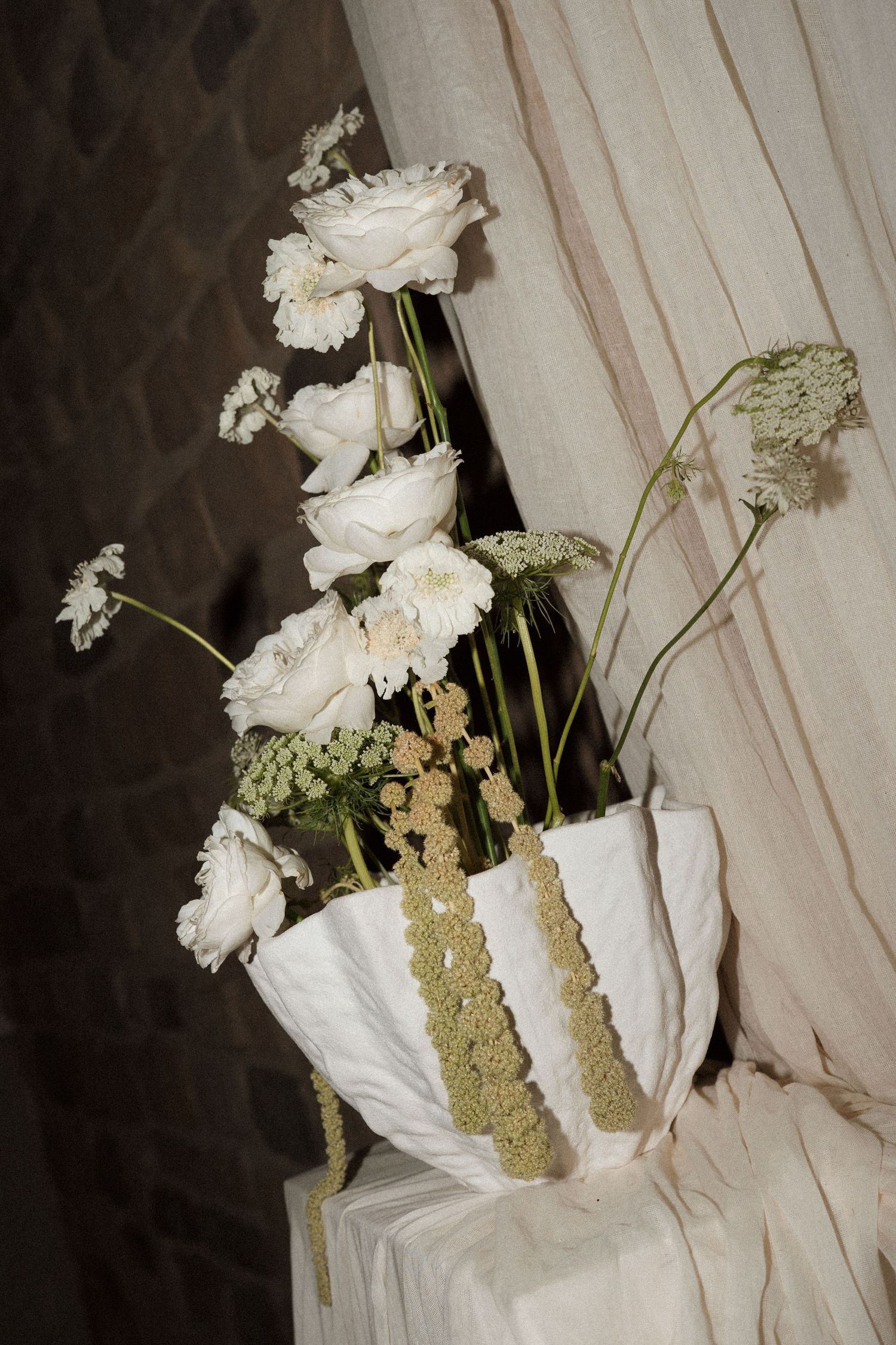 Elegant white floral arrangement with roses and greenery in a textured white vase.
