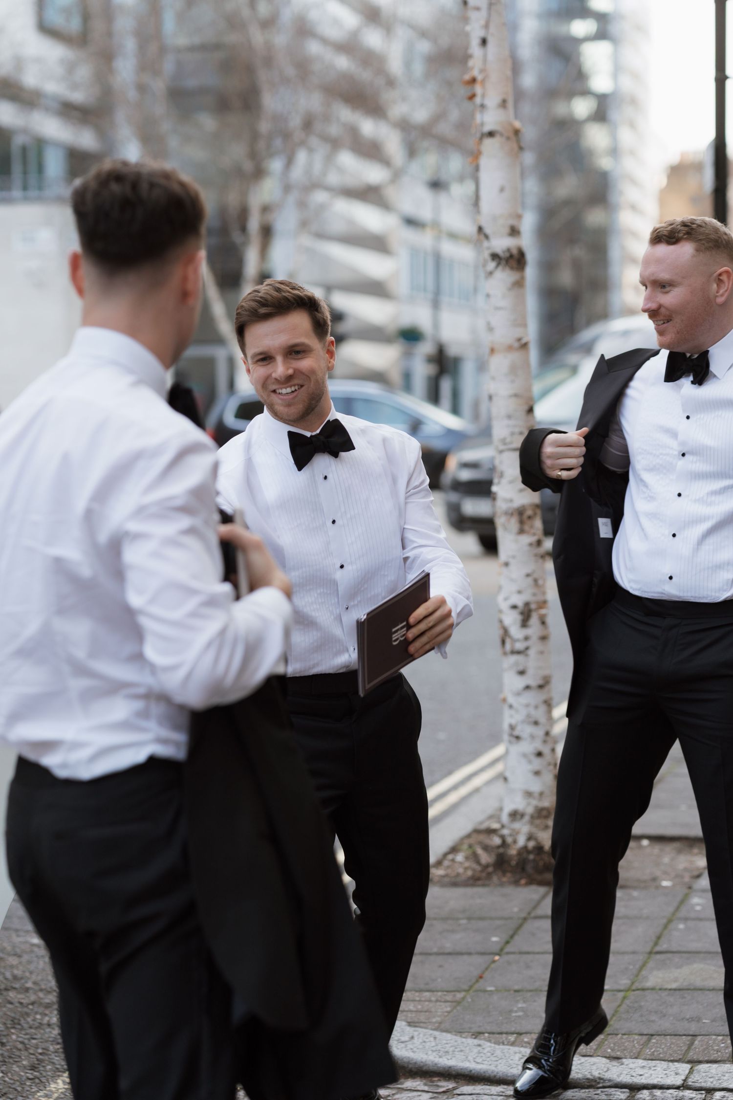 Groomsmen in formal black and white attire posing playfully outdoors.