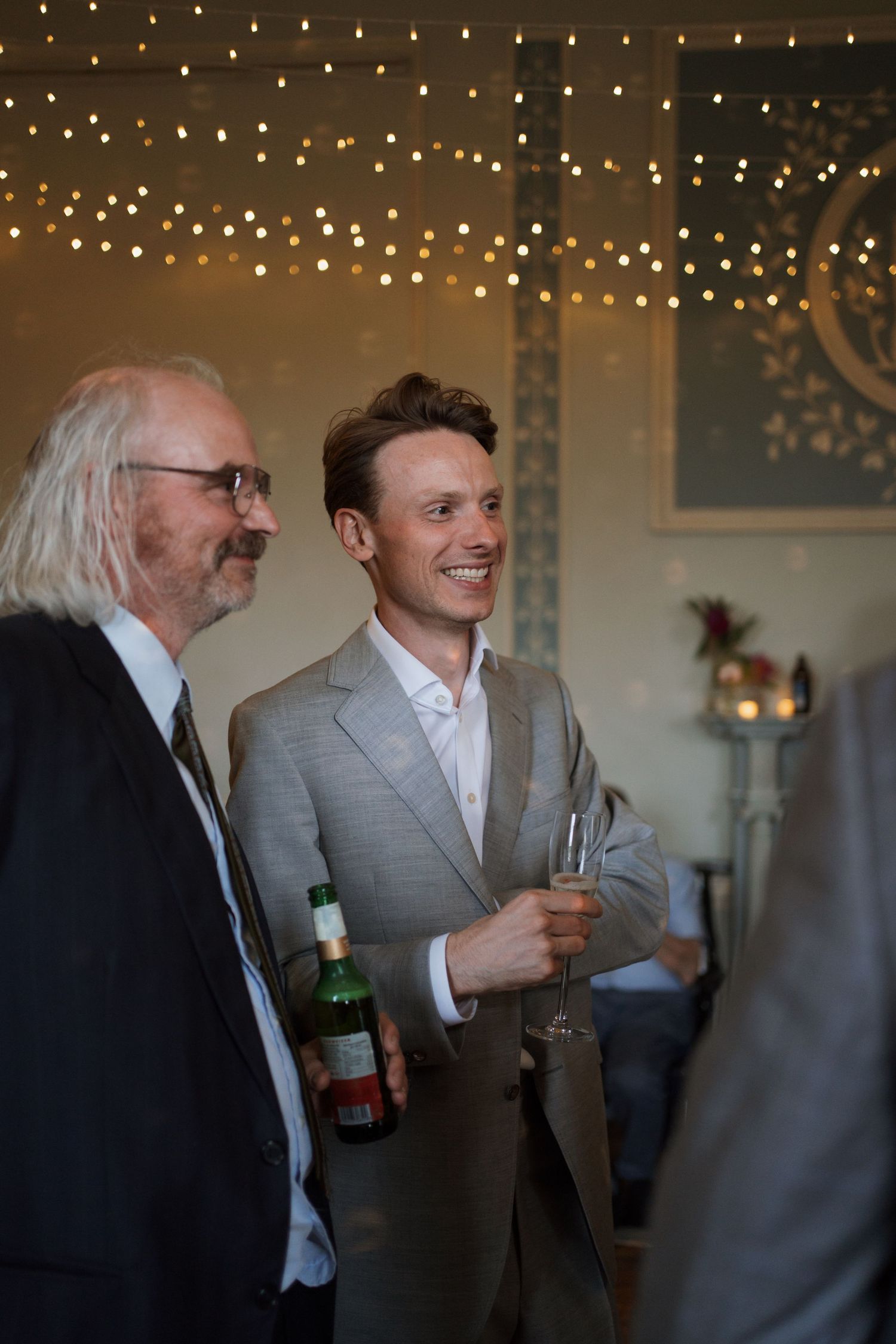 Wedding guests in formal attire sharing drinks and conversation under string lights.