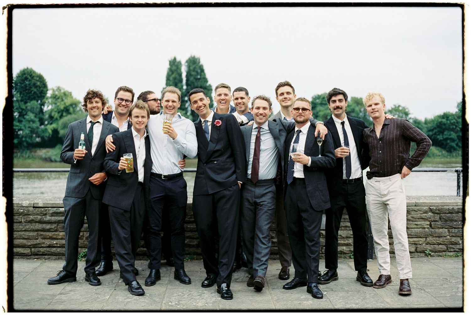 Large group of groomsmen in black suits posing together on stone steps.