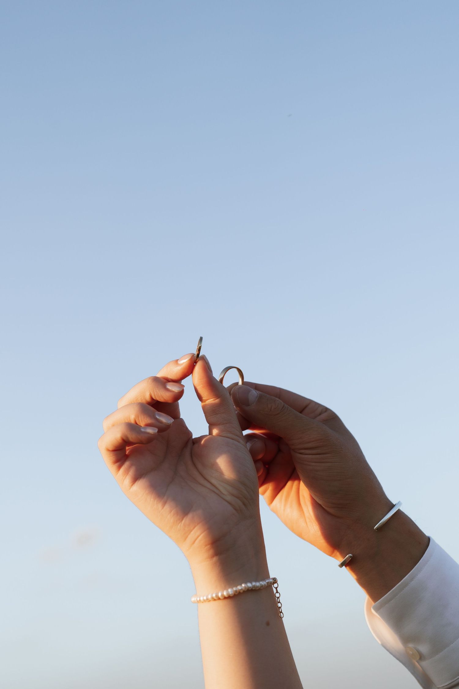 Close-up of hands against blue sky adjusting jewelry.