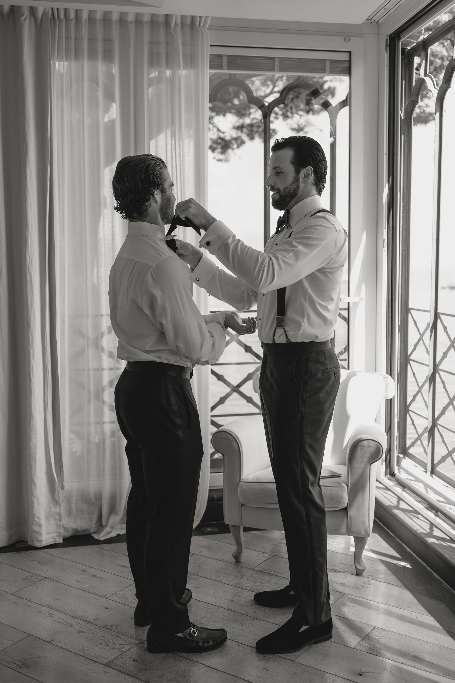 Black and white photo of formal preparation in a bright room with curtained windows.