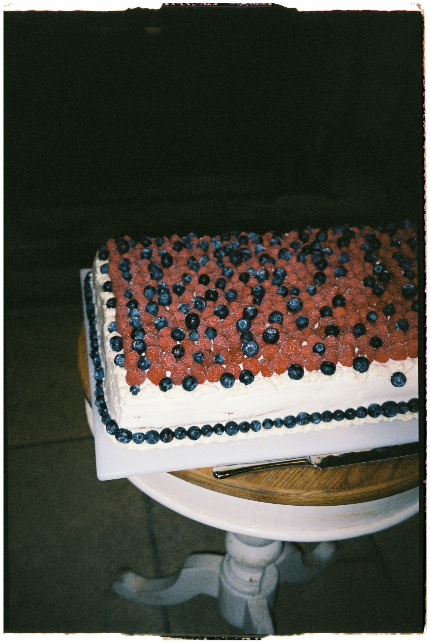 Wedding cake decorated with blue and coral colored berries along the edge.