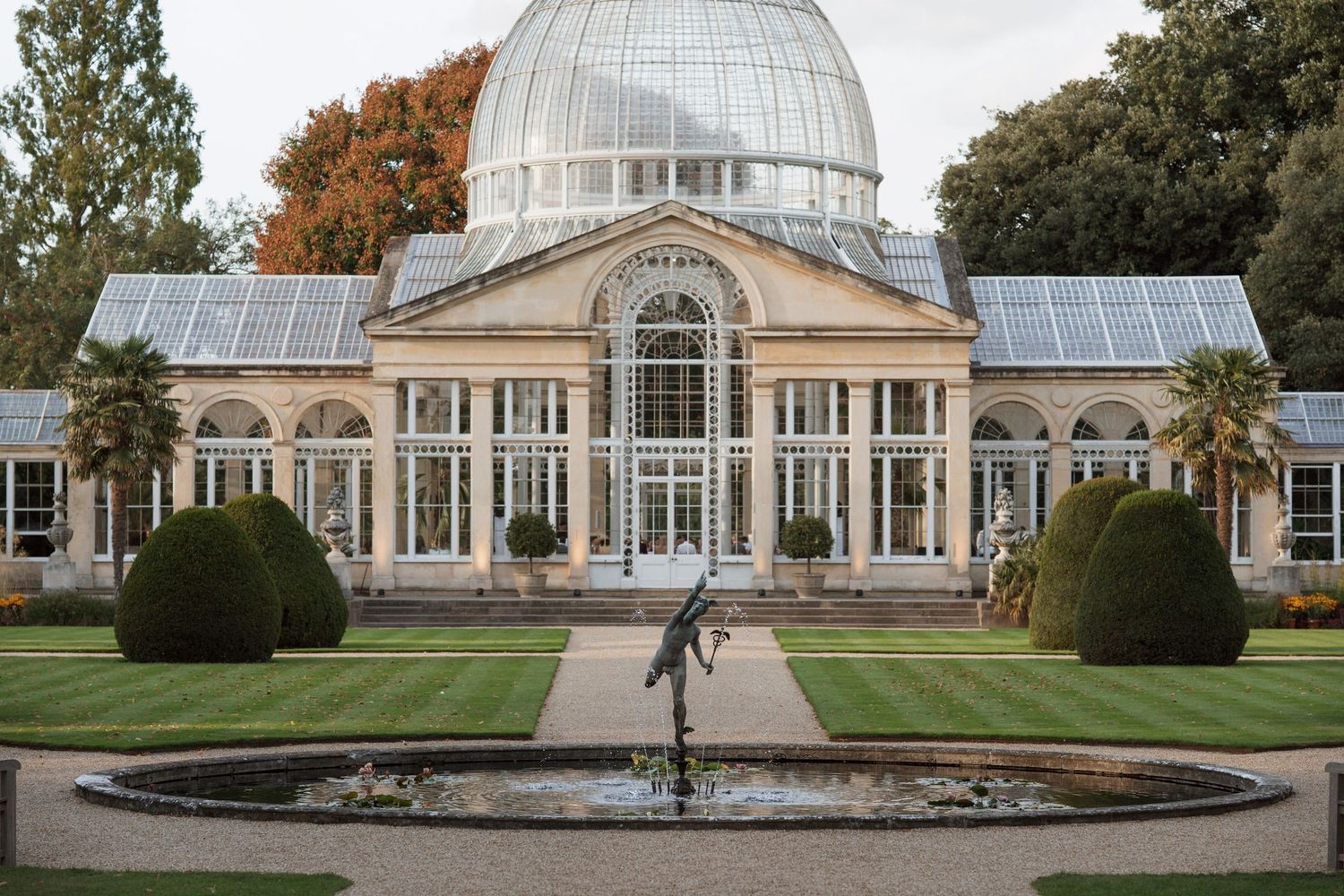 Grand conservatory building with glass dome and manicured lawns in daylight.