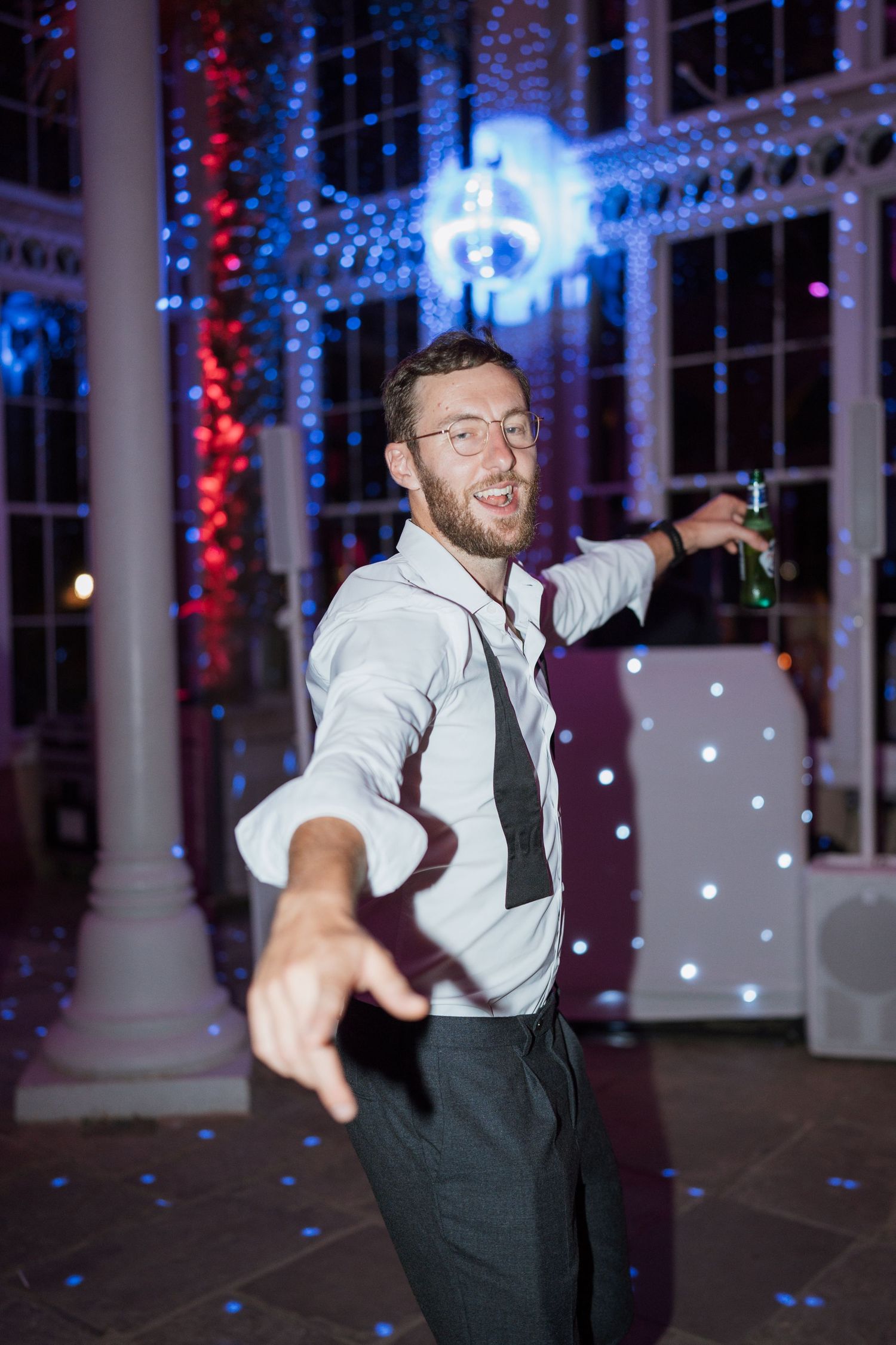 Person in white shirt and dark tie dancing energetically under blue party lights.