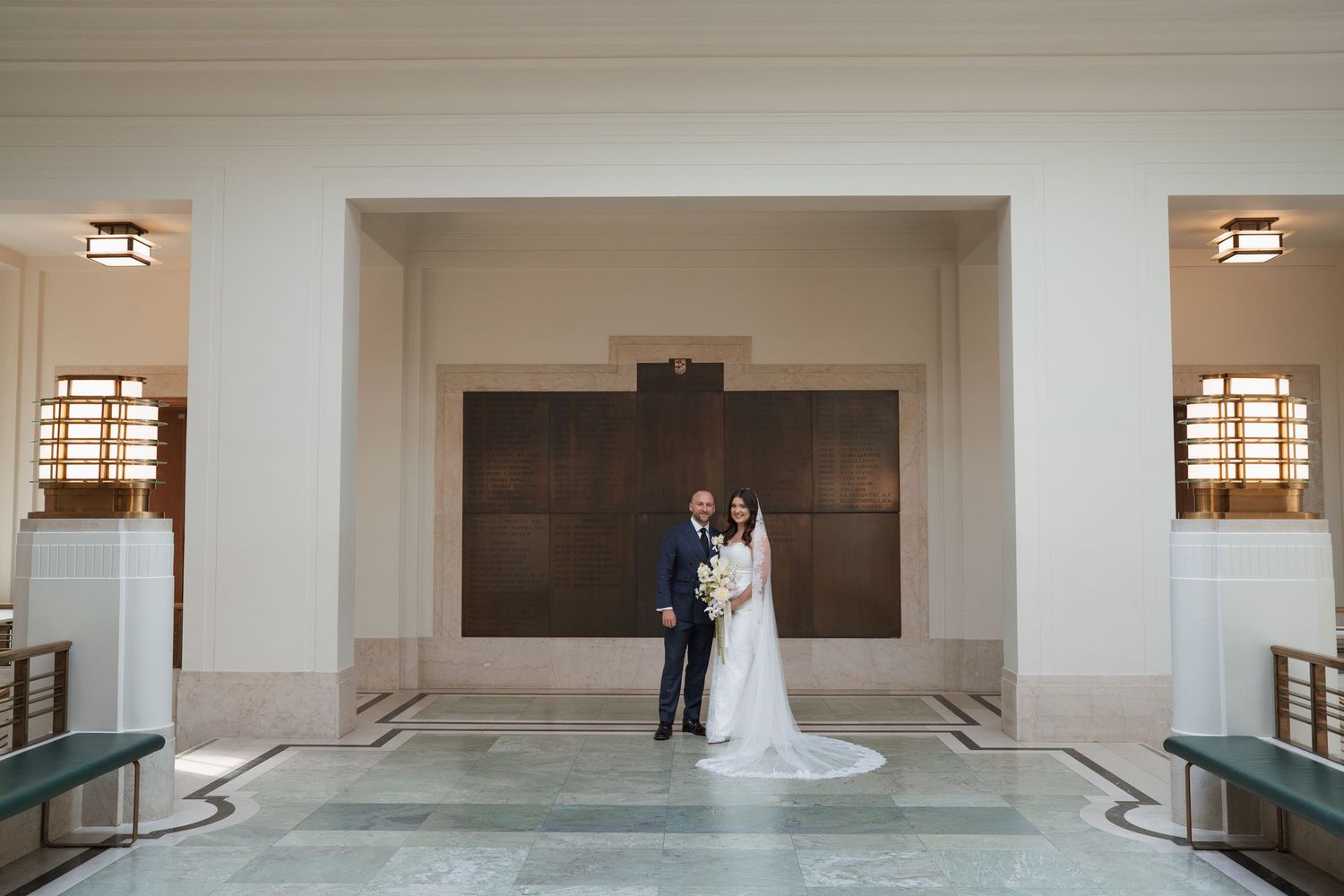 Bride and groom posing together in an elegant wedding venue lobby with marble floors and grand architectural details.
