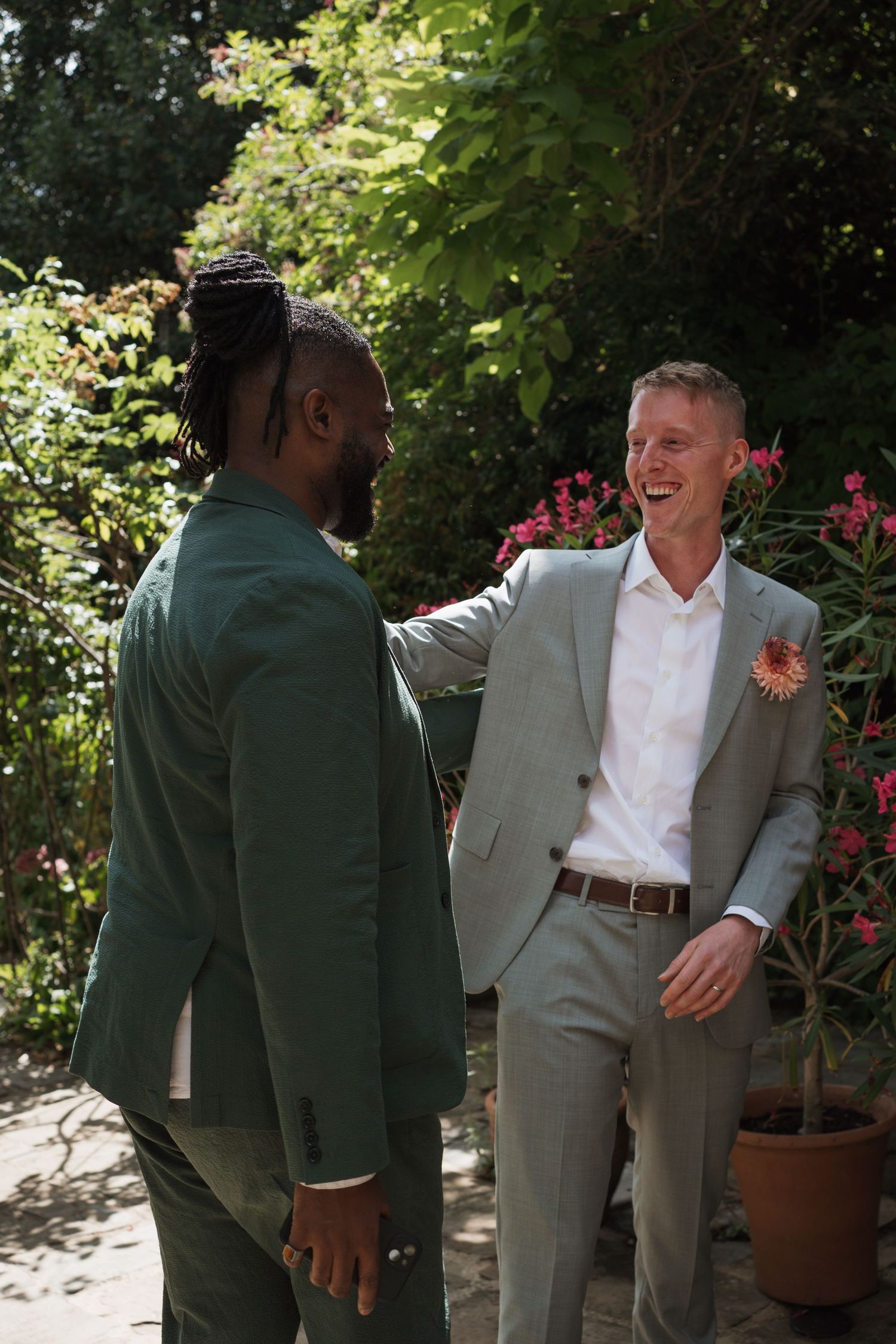 Wedding guests in formal attire interacting in a garden with blooming flowers.