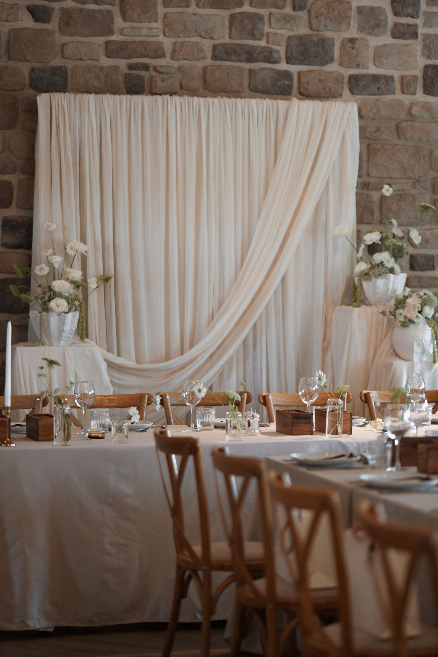 Wedding reception table setup with draped fabric backdrop and elegant place settings.