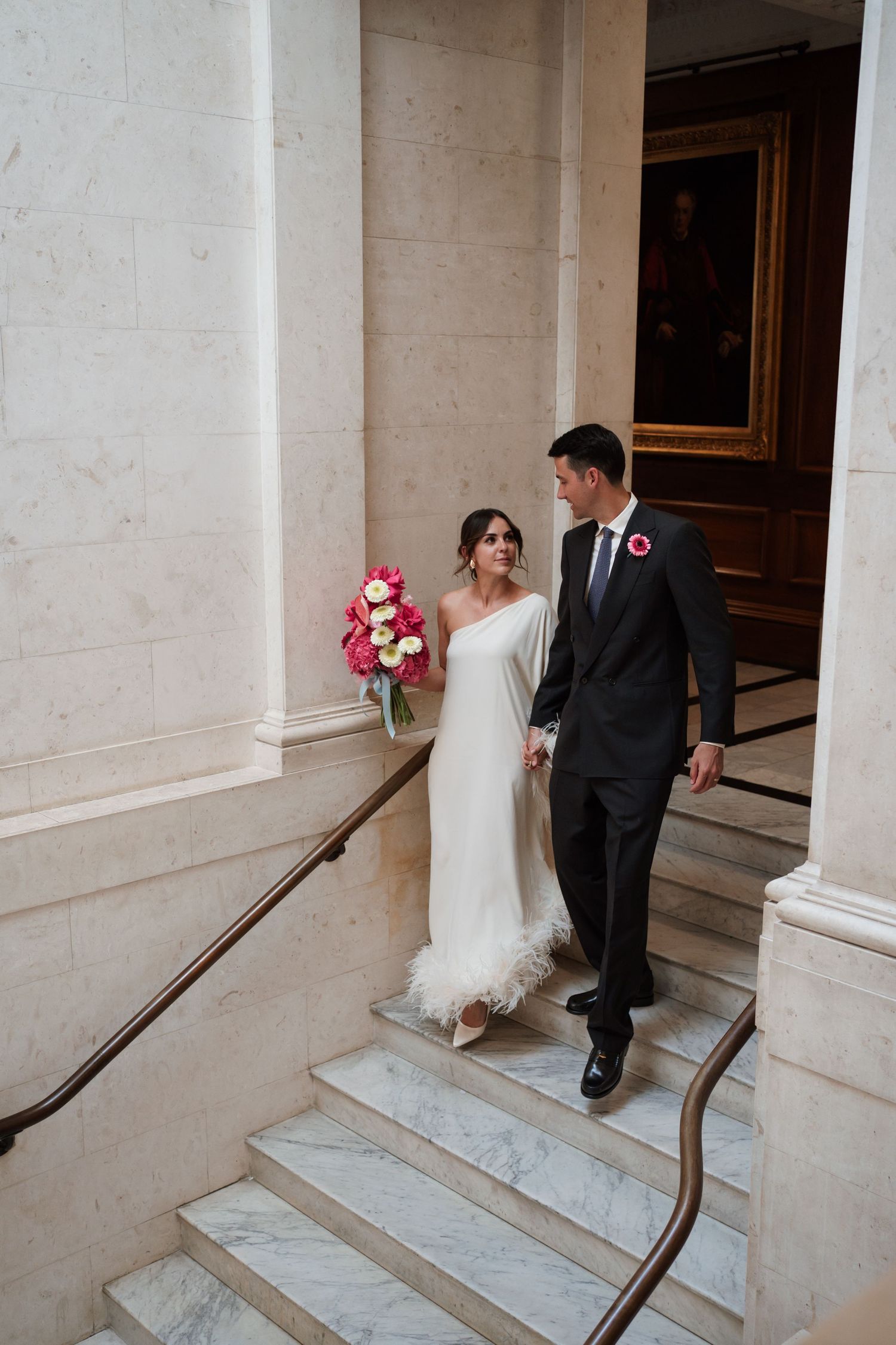 Wedding couple ascending marble steps at an elegant venue entrance.