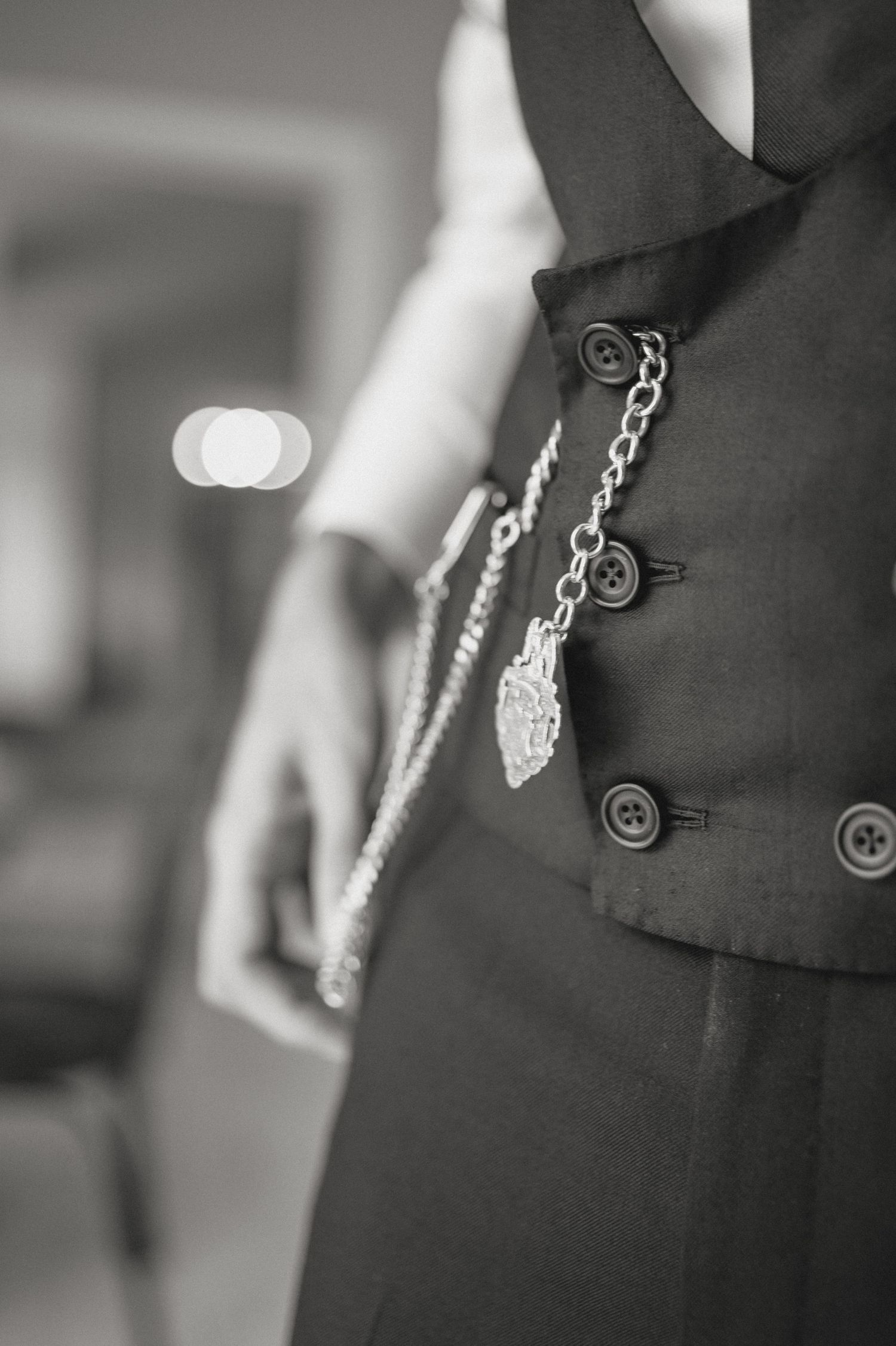 Decorative chain accessory hanging from black formal vest with buttons.