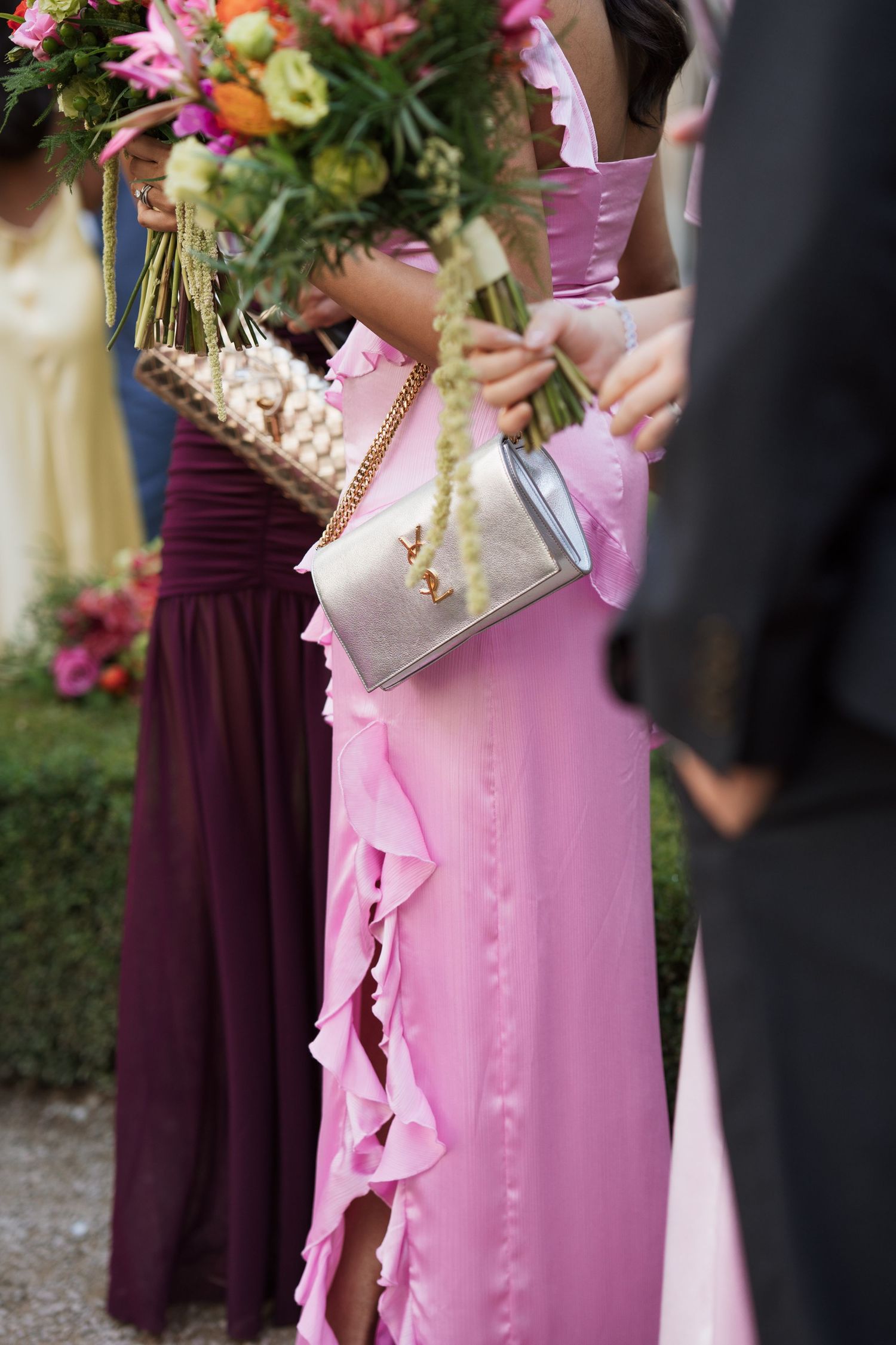 Wedding party members holding colorful bouquets wearing pink and burgundy dresses.